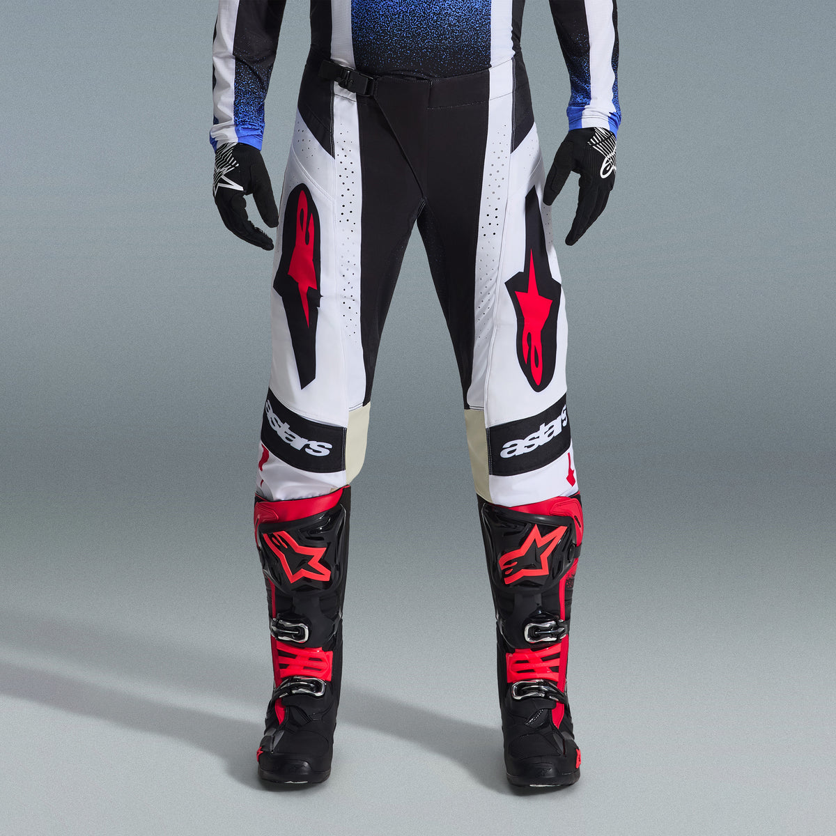 Ensemble d'équipement Alpinestars Techstar Knif 2026, équipement de motocross, pantalon noir et blanc avec de grands logos étoile rouges, porté avec des bottes de course noires et rouges et des gants noirs, coupe athlétique professionnelle pour la performance tout-terrain