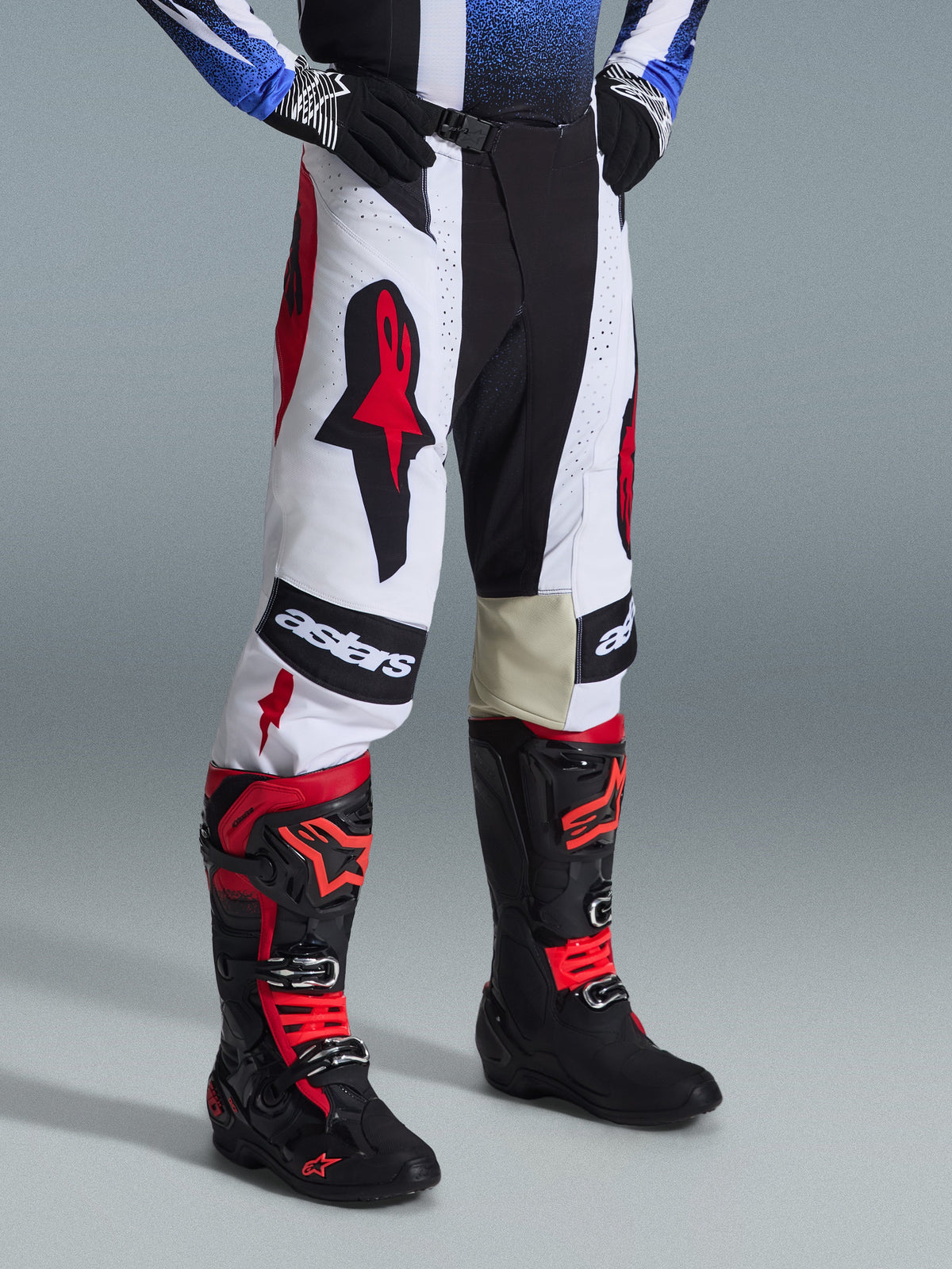 Ensemble d'équipement Alpinestars Techstar Knif 2026, pantalon et bottes de motocross, blanc, noir et rouge, avec logos audacieux et construction multi-matériaux, porté avec des gants noirs, équipement de course professionnel pour performance tout-terrain