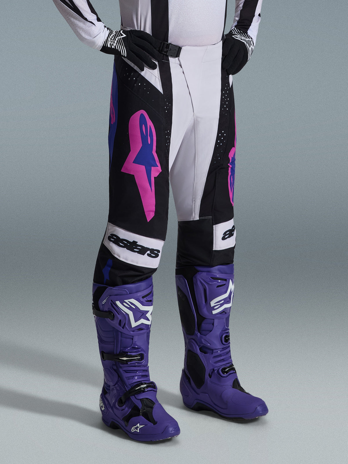 Alpinestars 2026 Techstar Knif Hose, Schwarz, Hellgrau und Lila, getragen mit passenden lila Motocross-Stiefeln, mit auffälligen pinkfarbenen Akzenten und „astars“-Branding, professionelle Motocross-Rennausrüstung