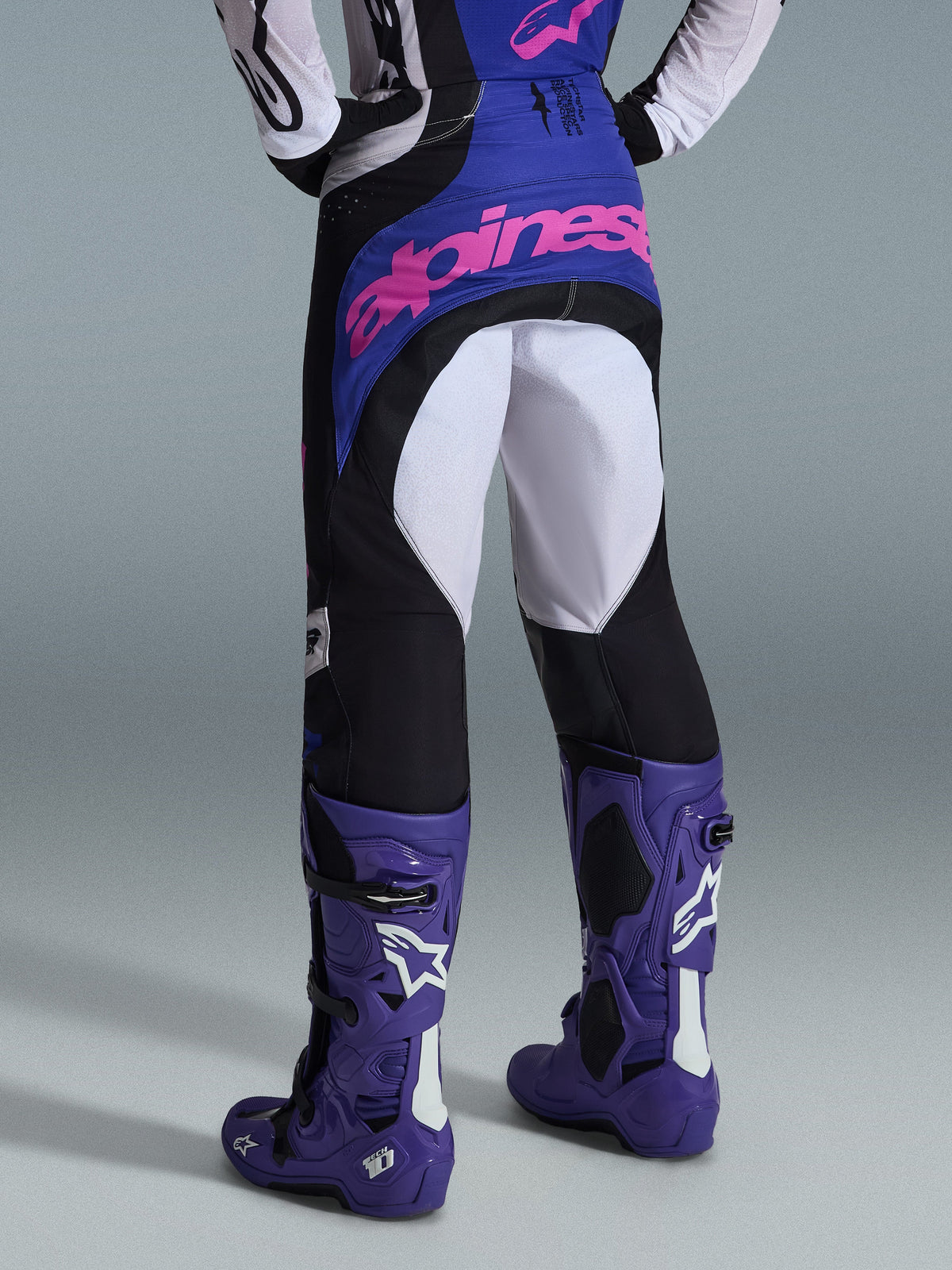 Alpinestars 2026 Techstar Knif Hose, Motocross-Hose, Schwarz, Hellgrau und Lila, Rückansicht mit pinkem Branding auf dem Gesäß, getragen mit passendem Trikot und lila Motocross-Stiefeln, professionelles Offroad-Rennoutfit