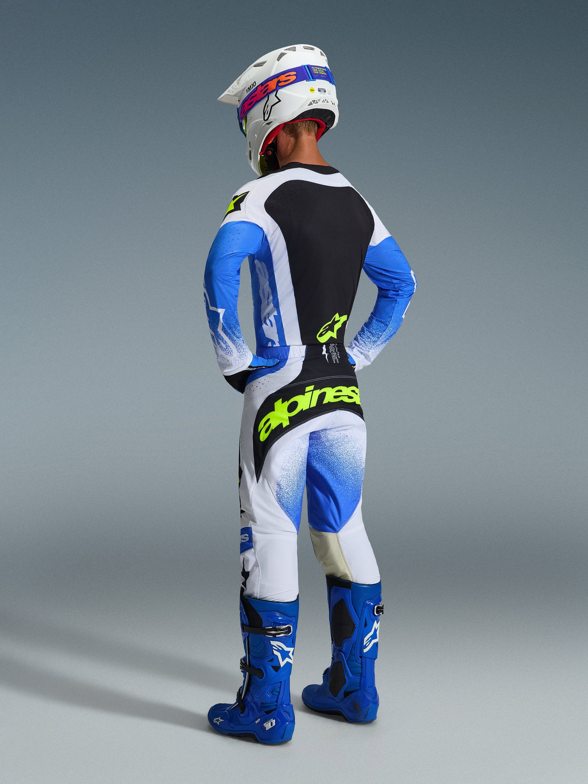 Pilote de motocross vu de dos portant le pantalon 2026 Techstar Knif en coloris Bleu Ucla, Noir et Jaune Fluo, avec logo jaune vif sur l'assise, maillot coordonné aux manches bleues, casque blanc et bottes tout-terrain bleues.