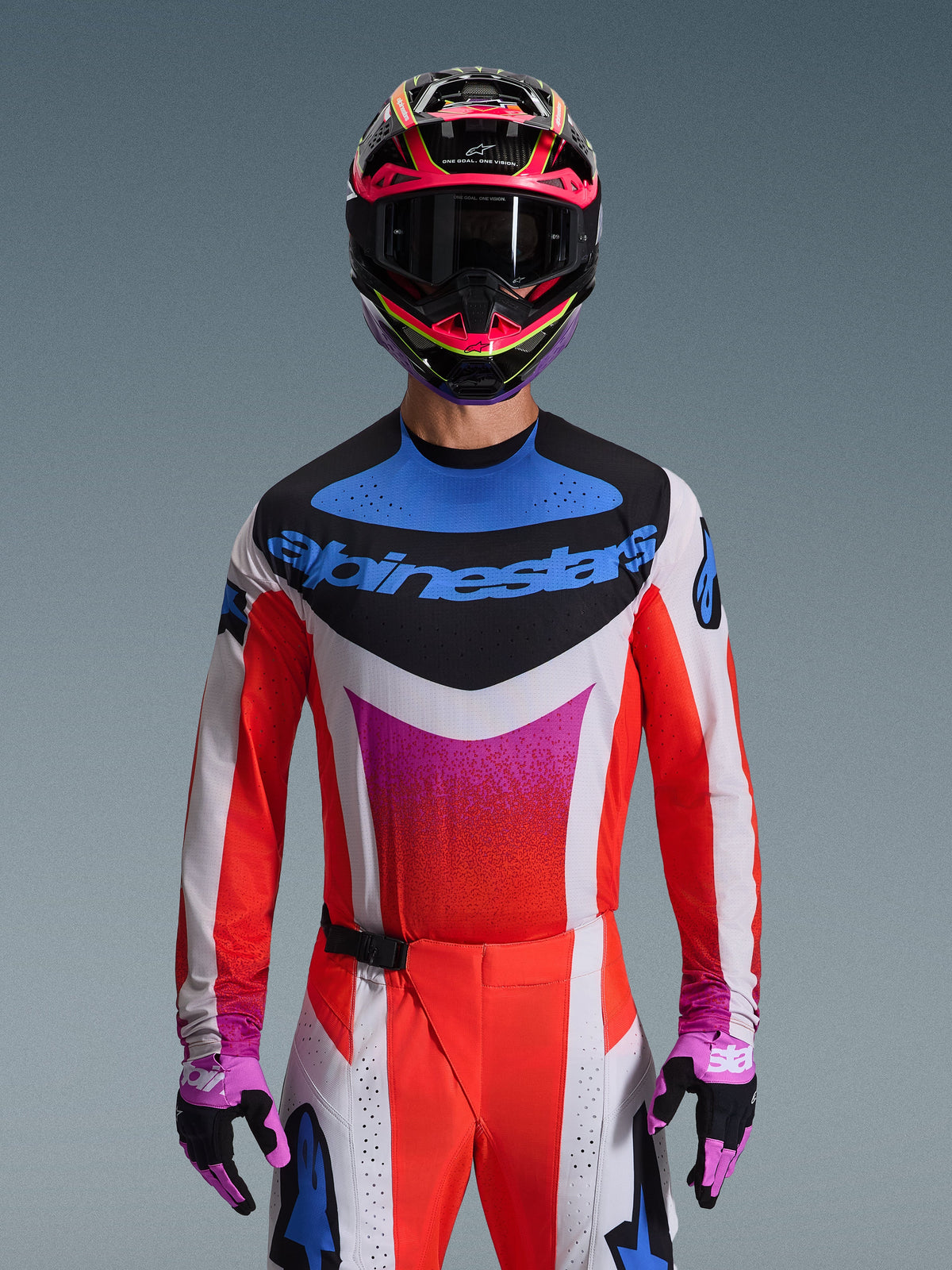 Motocrossrijder in de 2026 Techstar Knif Gear Set, witte jersey met rode mouwen en een blauwe en roze graphic op de borst, bijpassende rood-witte broek, opvallende roze en gele helm met donkere bril en paars-zwarte handschoenen, professionele uitrusting voor off-road racen.