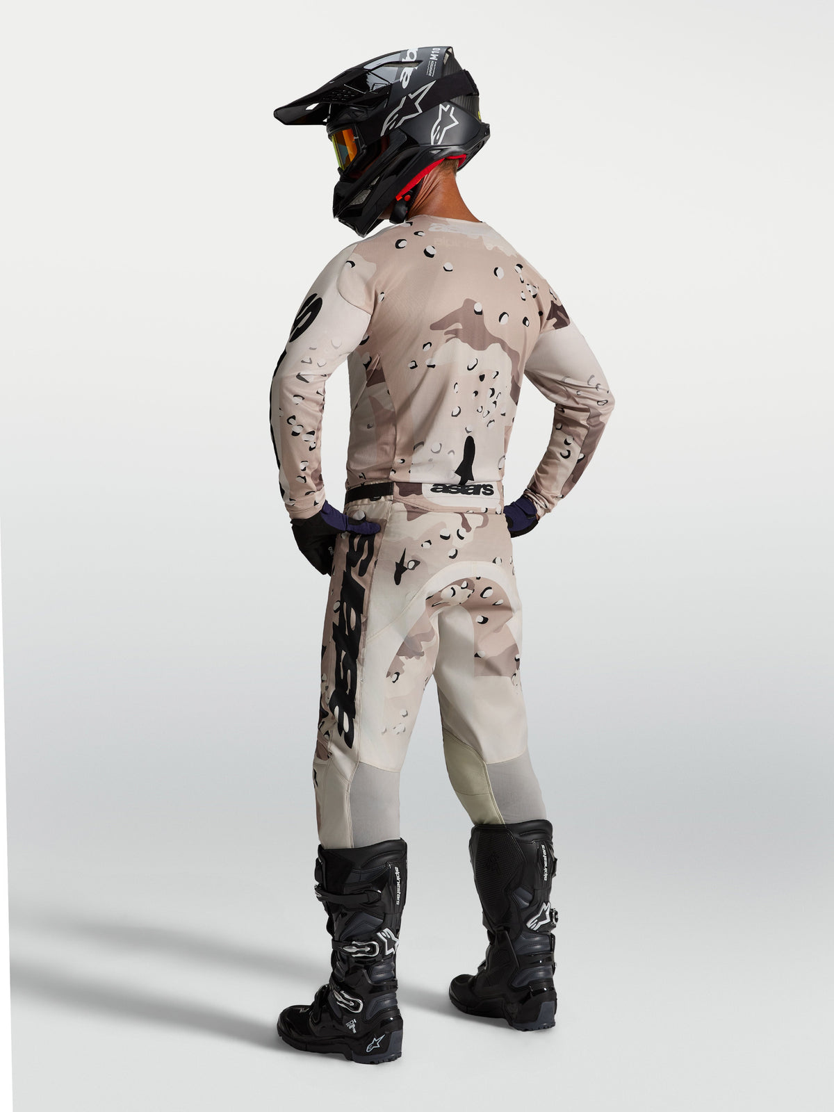 Alpinestars Racer Lone gear set, zandkleurige camouflage motocrossjersey en broek, achteraanzicht met zwarte motorlaarzen.