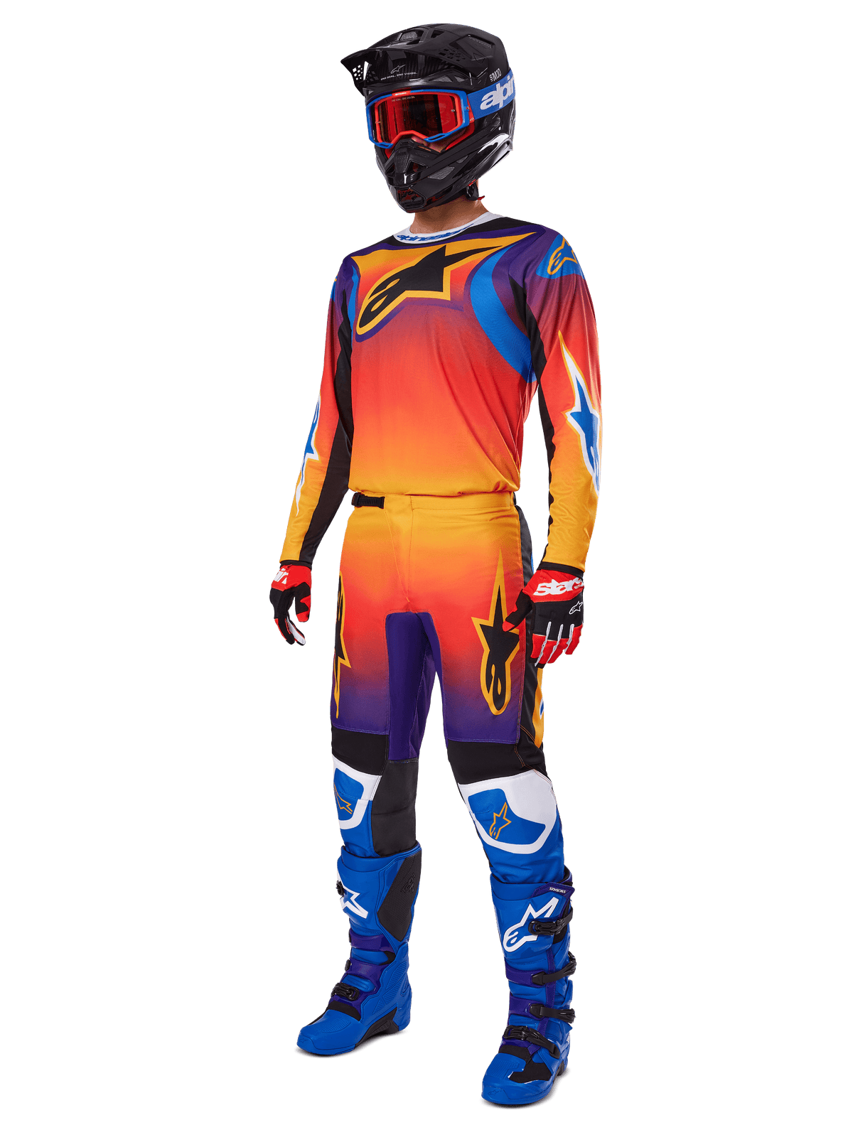 Motocross rider wearing complete racing gear, Alpinestars 2025 Fluid Wurx Pants and matching jersey in a multicolor orange, red, and purple gradient, black helmet with red goggles, blue and black boots, red and black gloves, coordinated outfit for off-road racing