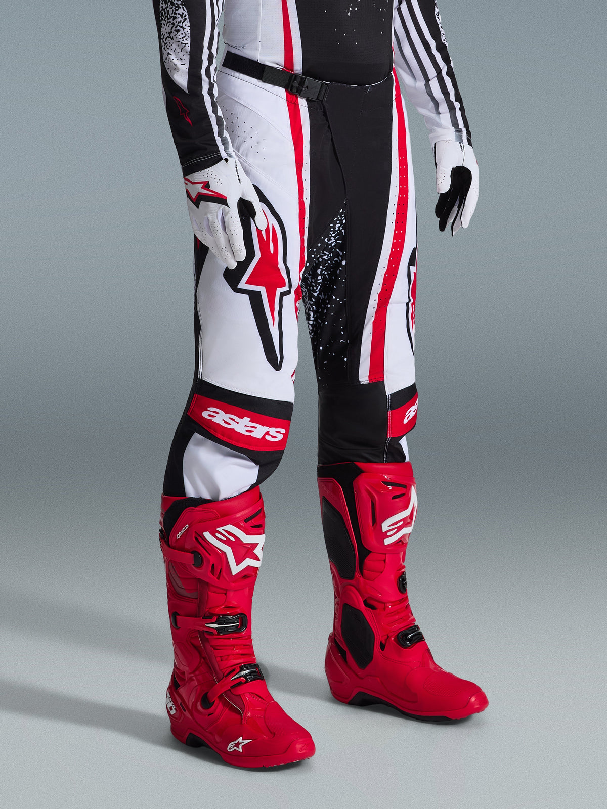 Alpinestars 2026 Techstar Nomur Hose, Motocross-Hose, Schwarz Weiß Rot, getragen mit leuchtend roten Rennstiefeln und weißen Handschuhen, mit markanten vertikalen Streifen, einem großen roten Stern-Logo auf dem Oberschenkel und verstärkten Knieeinsätzen für Offroad-Performance.