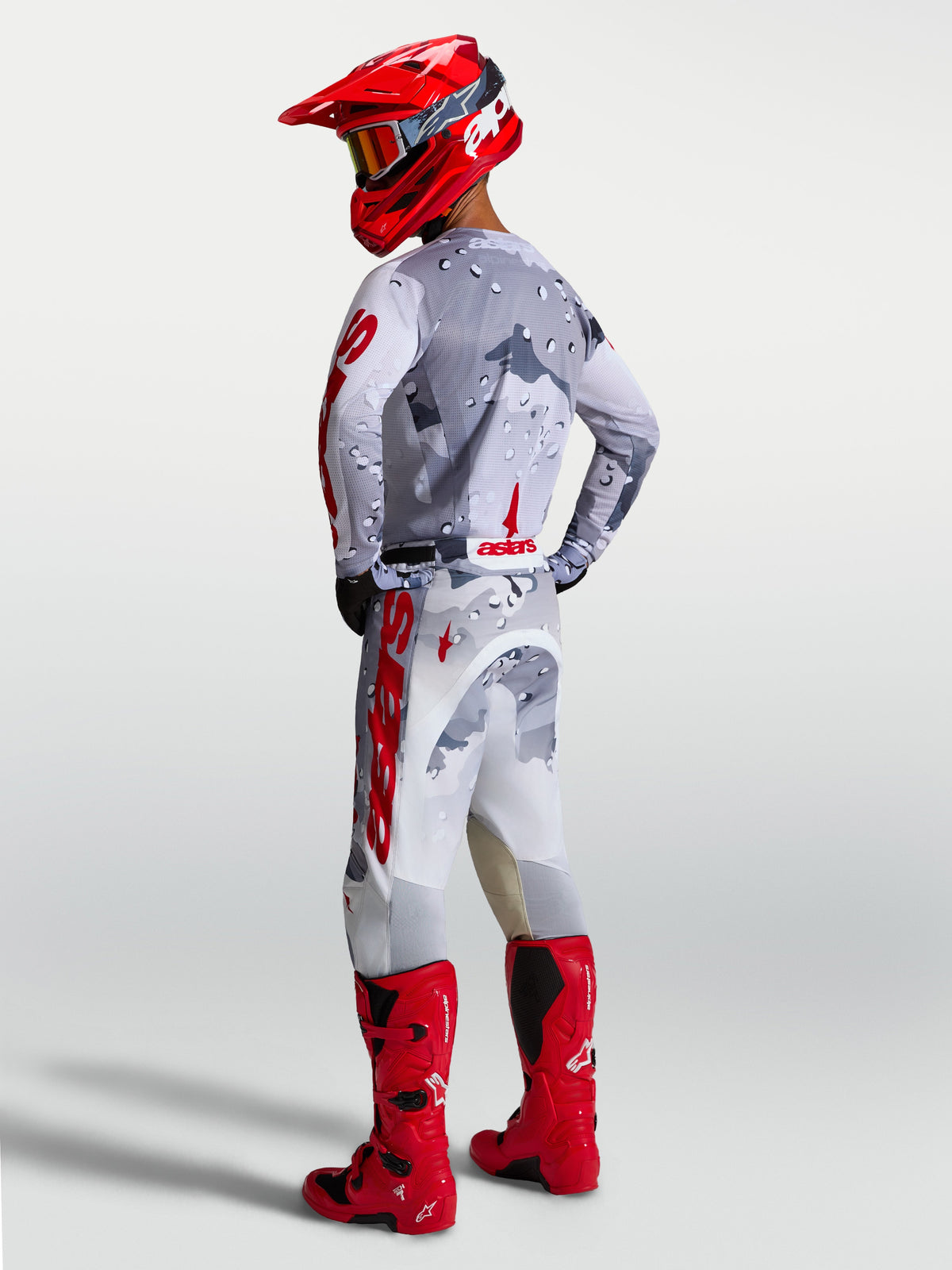 Pantalon Racer Air Lone Alpinestars, pantalon de motocross pour homme, gris camouflage et rouge, équipement ventilé avec stretch de performance, vue de dos porté par un pilote avec bottes et casque rouges