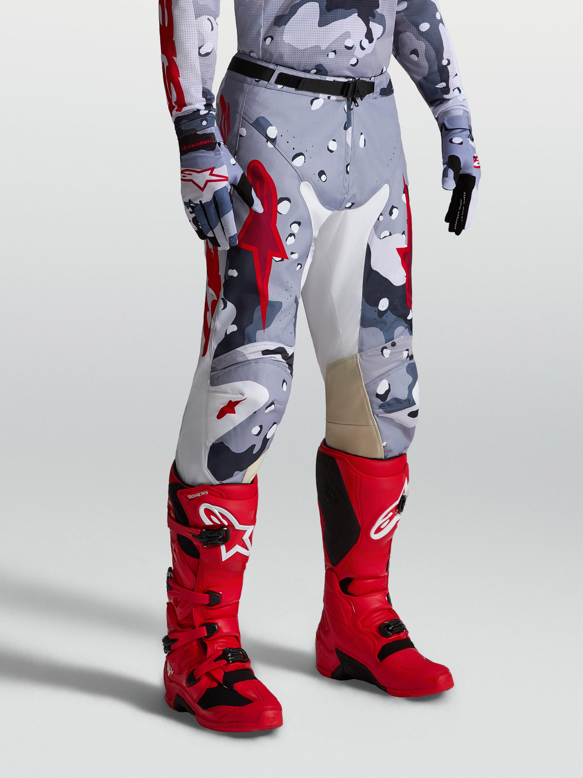 Alpinestars Racer Air Lone broek, geperforeerde motorcrossbroek voor off-road terreinrijden, grijs camouflage en rood ontwerp, getoond op een model.
