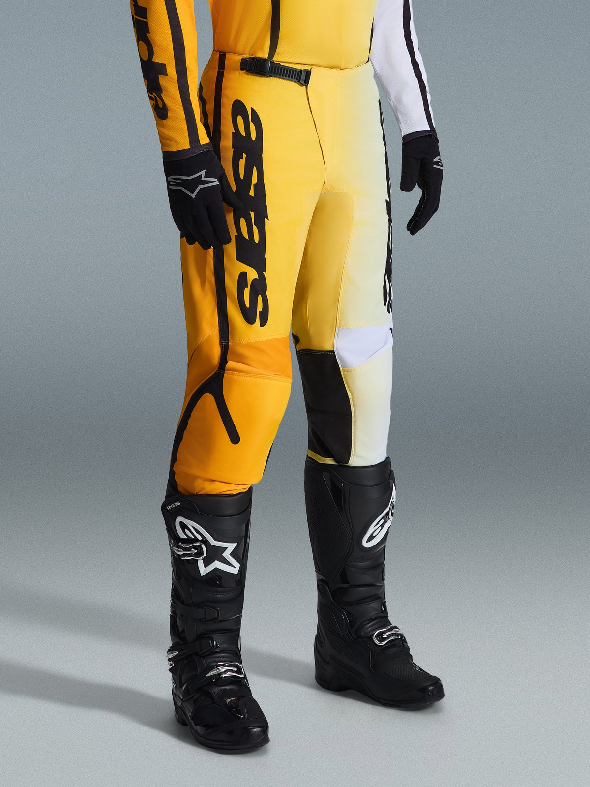 Alpinestars 2026 Fluid Apex crossbroek, motorcrossbroek, geel en zwart, gedragen met zwarte laarzen en handschoenen, voorzien van opvallende 'astars' branding op het dijbeen, ergonomisch ontwerp met versterkte panelen, duurzaam materiaal voor off-road rijden