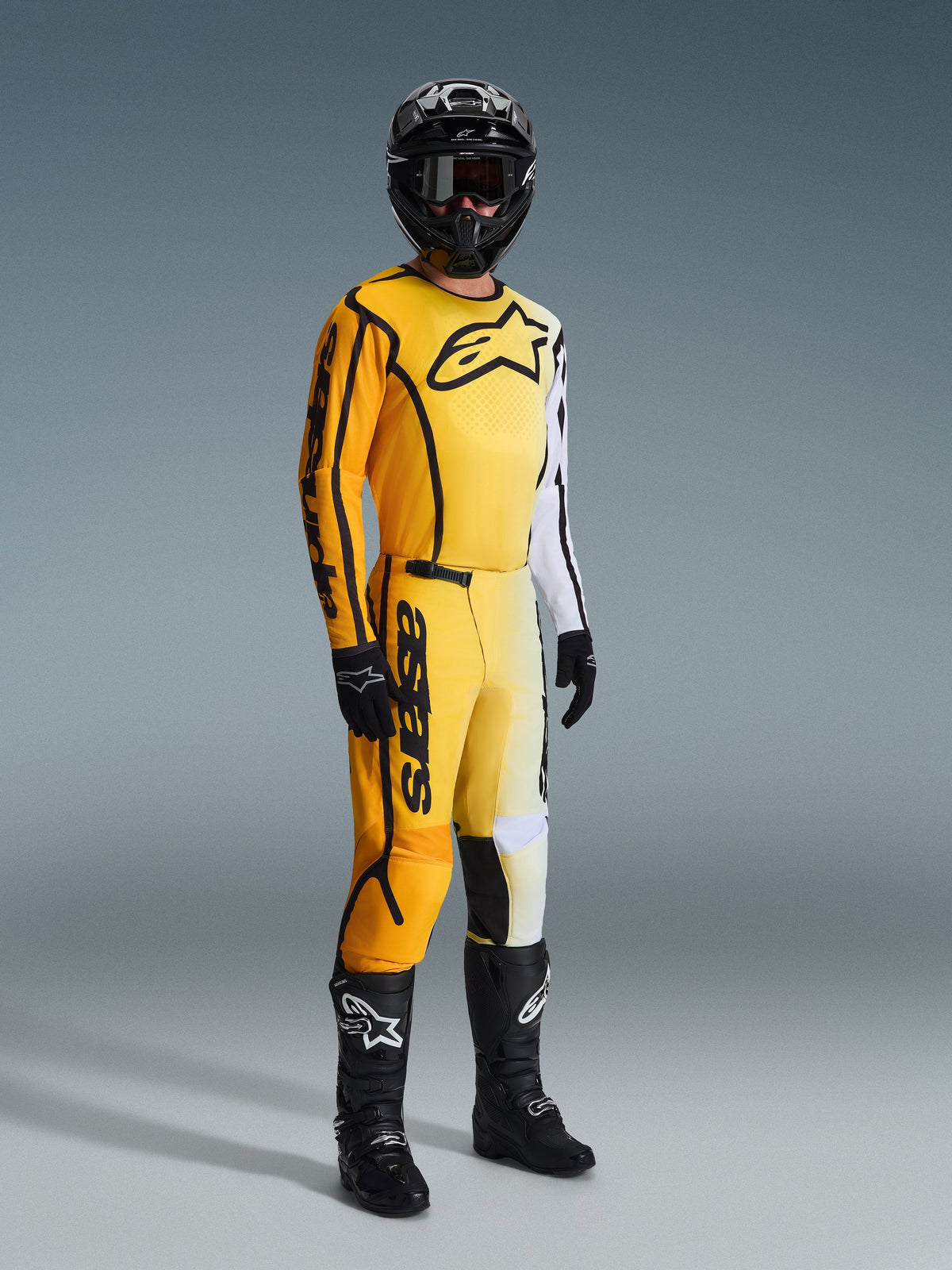Alpinestars 2026 Fluid Apex broek, motorcrossbroek, geel en zwart, gedragen met bijpassende geel-witte jersey, zwarte helm, bril, handschoenen en zwarte laarzen, met opvallende zwarte branding en een modern kleurverloop voor off-road racen.