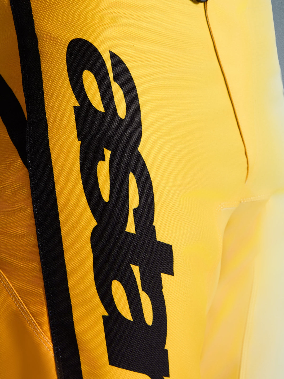 Close-up van Alpinestars 2026 Fluid Apex crossbroek, motorcross broek, geel en zwart, met een groot verticaal zwart logo, getextureerd duurzaam materiaal en ergonomische details voor off-road prestaties