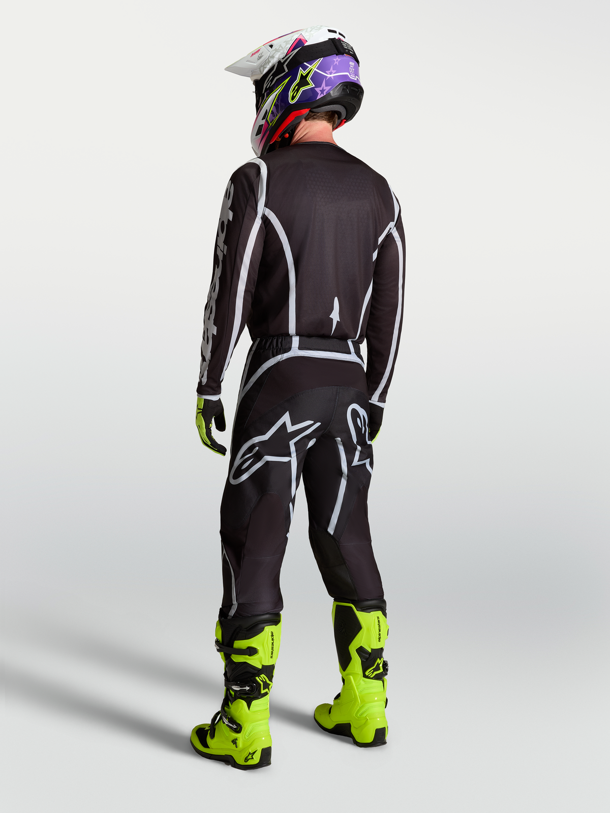 Pantalon Alpinestars Fluid Apex V2, équipement de motocross pour homme, noir et argenté, vue de dos avec maillot assorti et bottes jaune fluo.