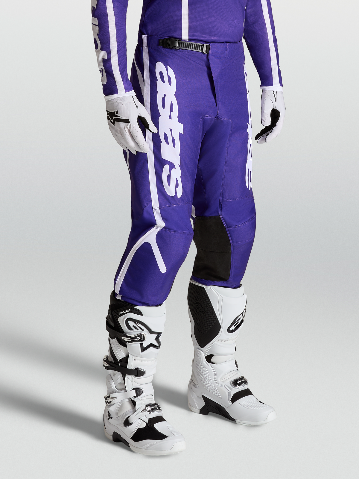 Alpinestars Pantalon Fluid Apex V2, équipement de motocross pour homme, bleu et blanc, jambes pré-courbées, porté avec bottes et gants blancs