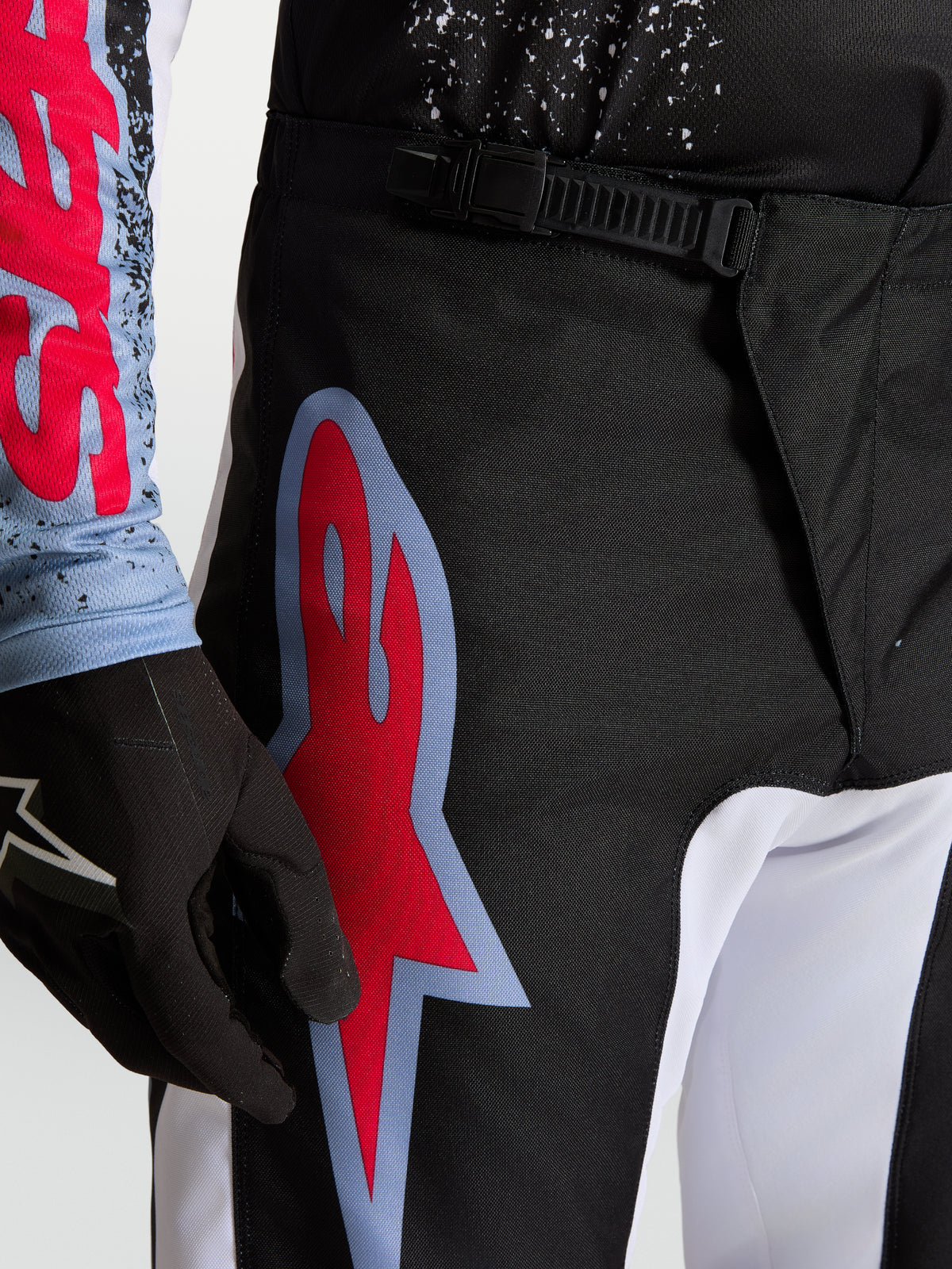 Alpinestars Fluid Drag broek, heren motorcrossbroek in zwart en rood, voorzien van een ratelsluiting en een groot grafisch logo.