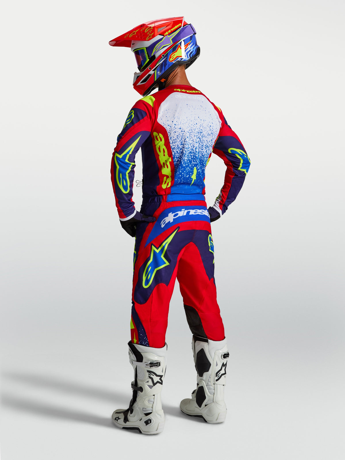 Alpinestars Fluid Drag broek en 2027 Fluid Drag gearset, blauw en rood heren motocrosspak met witte laarzen, achteraanzicht.