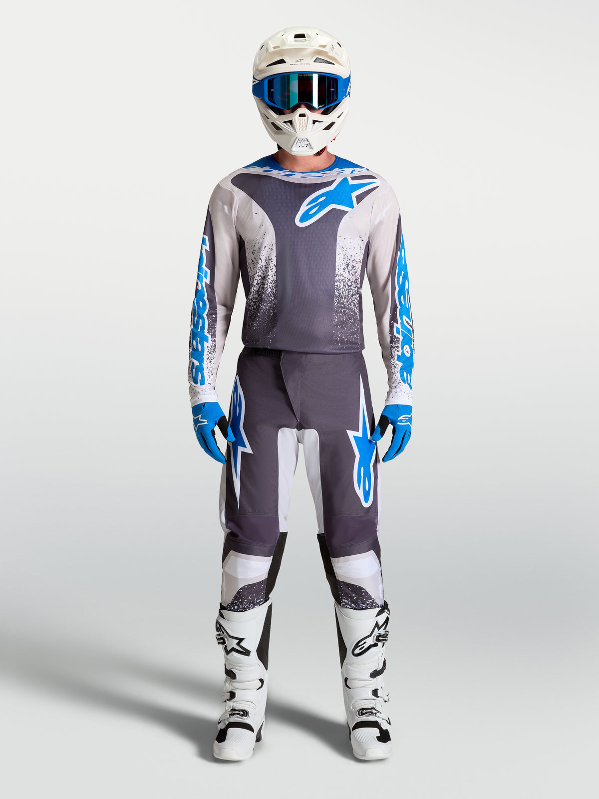 Alpinestars pantalon Fluid Drag, pantalon de motocross pour homme, gris et bleu, porté avec maillot et bottes blanches.