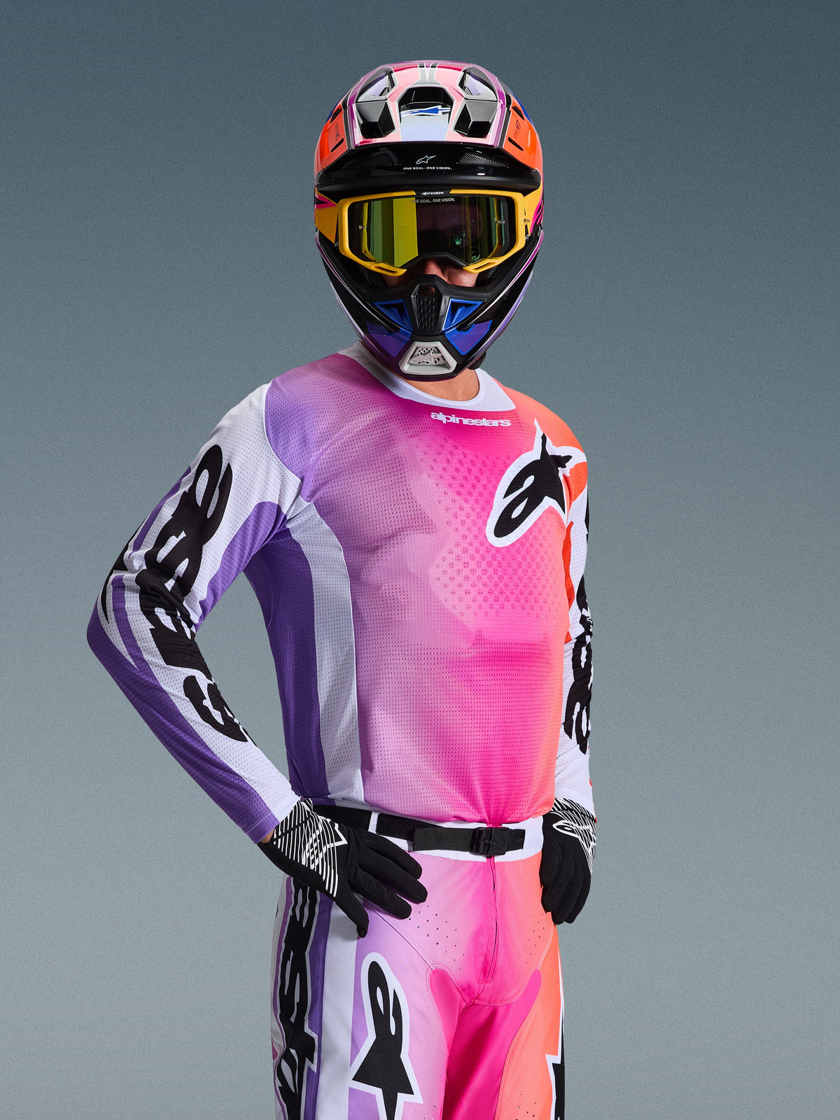 Pilote de motocross portant le maillot Alpinestars Racer Air Portl 2026, dégradé multicolore rose, violet et orange avec des accents blancs, casque coloré assorti et masque jaune, gants noirs, équipement de course tout-terrain professionnel