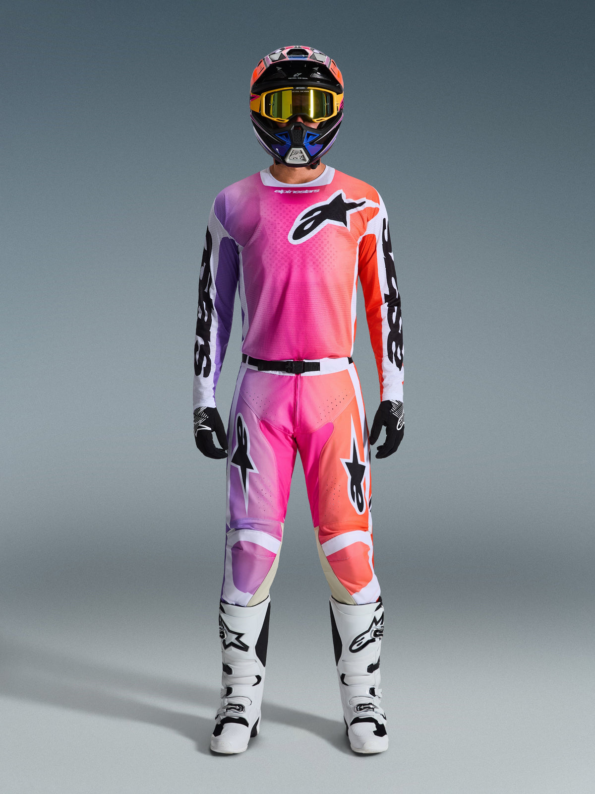 Tenue de motocross Alpinestars complète, maillot Racer Air Portl 2026 et pantalon assorti avec dégradé rose, violet et orange, logos Alpinestars noirs, bottes blanches, gants noirs et casque multicolore, équipement professionnel de course tout-terrain.