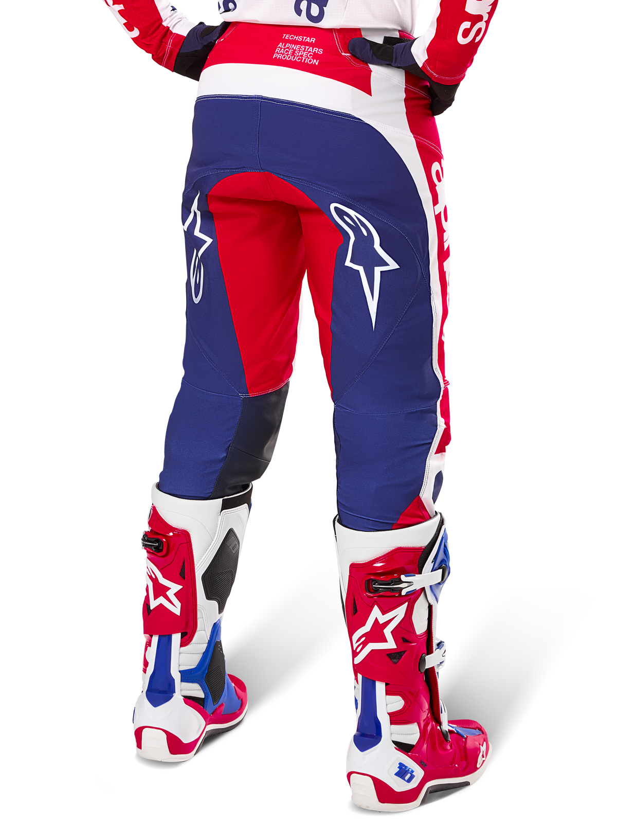 Alpinestars Limited Edition Techstar Fortitude broek, motorcrossbroek, rood, wit en blauw, achteraanzicht gedragen met bijpassende rode en witte laarzen, voorzien van witte sterlogo's op de dijen, duurzaam meerpaneel-ontwerp voor professioneel off-road racen.