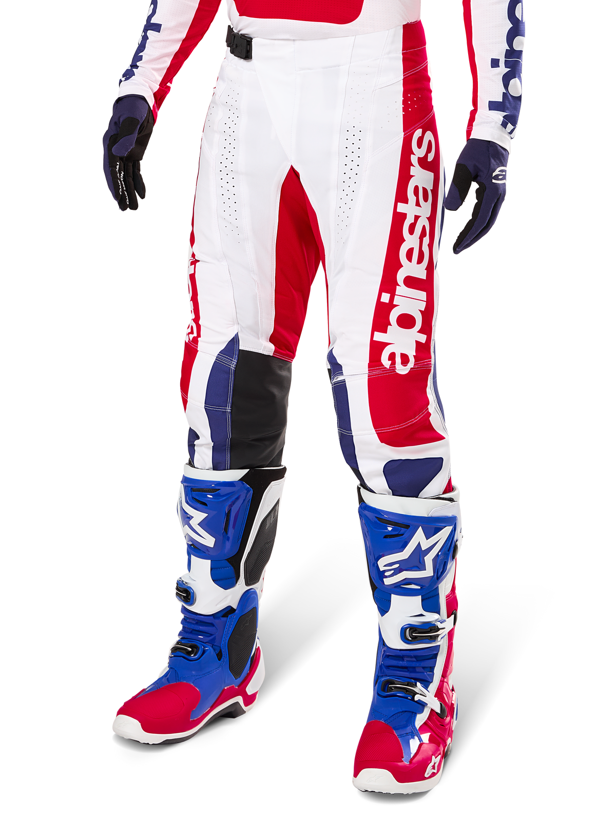 Alpinestars Limited Edition Techstar Fortitude crossbroek, motorcross broek, helder rood, wit en blauw, gedragen met bijpassende off-road laarzen en handschoenen, voorzien van verticale branding op de broekspijp, ademende geperforeerde panelen en zwarte verstevigde kniestukken, atletisch race-ontwerp