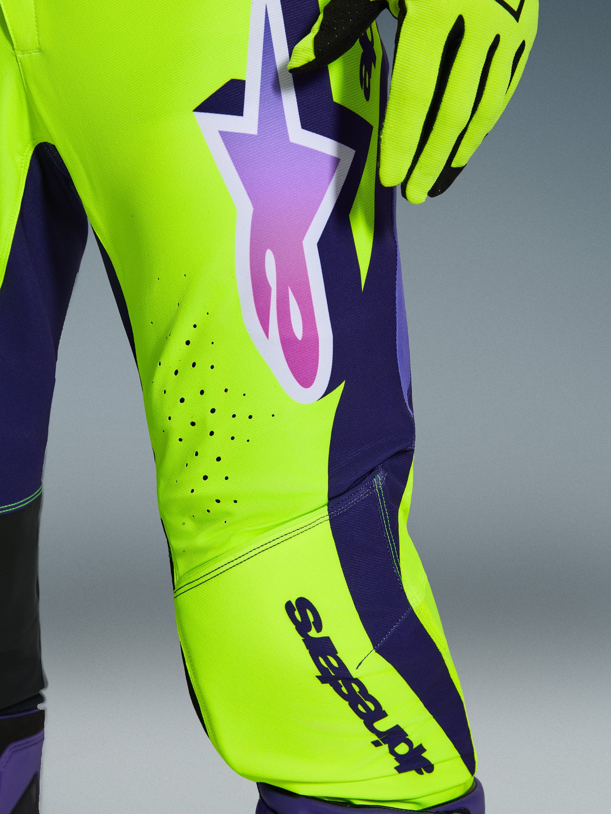 Pantalon Alpinestars Supertech Vista 2026, pantalon de motocross, jaune, violet et noir, vue rapprochée de la jambe montrant des panneaux jaune fluo et violet foncé, grand logo étoile violet en dégradé, perforations de ventilation découpées au laser, équipement de course professionnel