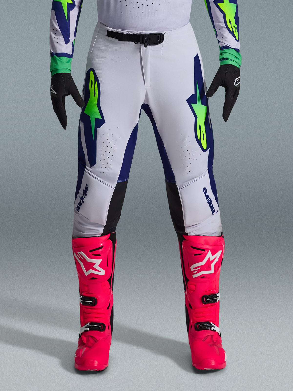 Alpinestars 2026 Supertech Vista Gear Set, pantalon de motocross blanc avec accents bleu et vert citron, associé à des bottes rose vif et des gants noirs, équipement de course professionnel avec coupe athlétique et perforations au laser.
