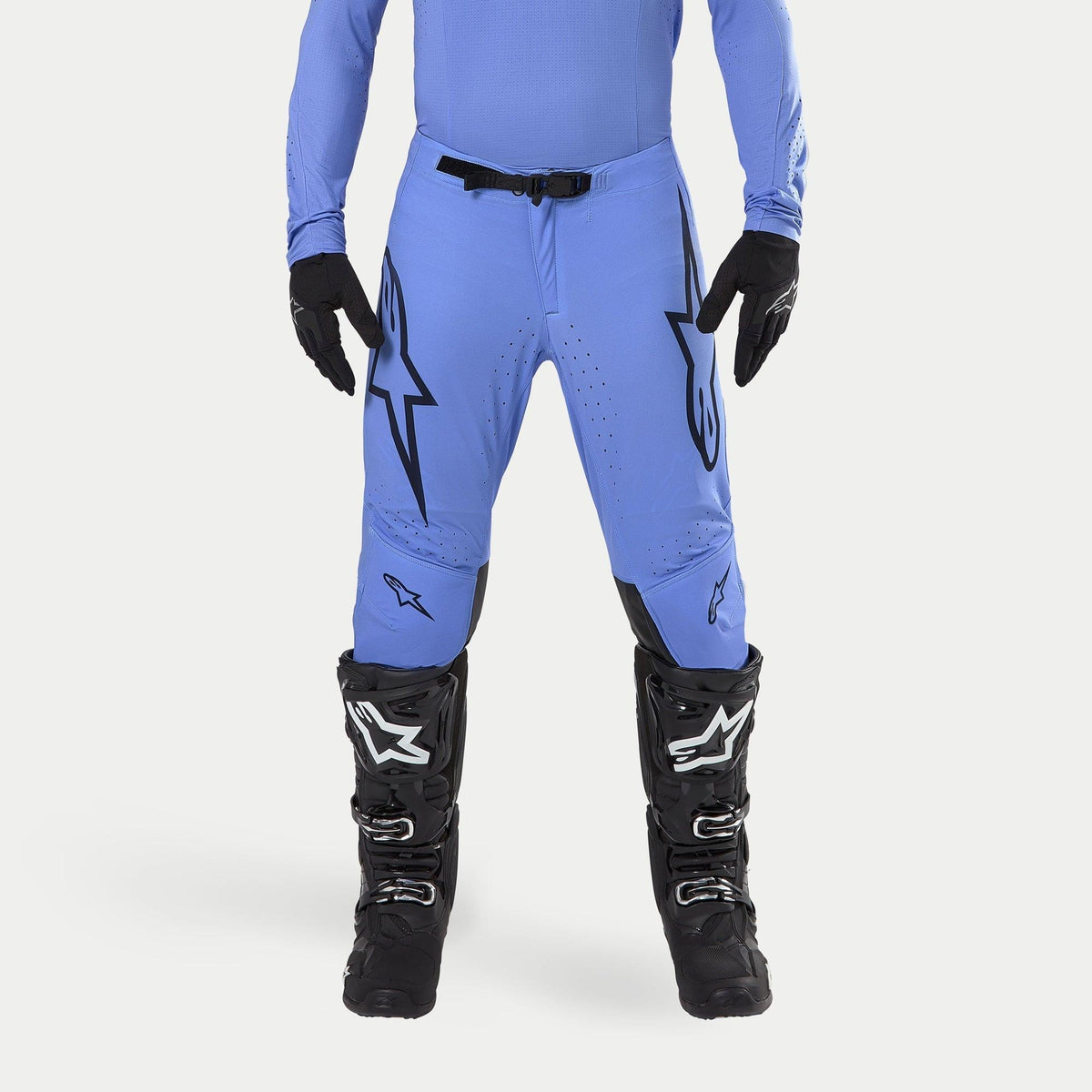 Pantalon Alpinestars Supertech Dade 2024, pantalon de motocross, bleu clair, avec de grands logos Astars noirs sur les cuisses, boucle de taille noire, porté avec des bottes de motocross noires et un haut bleu assorti, vêtement de course tout-terrain professionnel