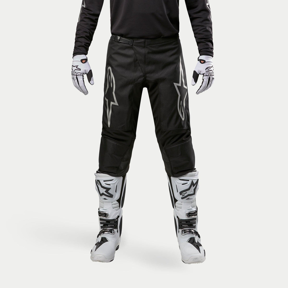 Alpinestars 2024 Fluid Graphite Hose, Motocross-Hose, Schwarz und Silber, mit silbernen Alpinestars-Logos auf den Oberschenkeln, getragen mit weiß-schwarzen Motocross-Stiefeln und Handschuhen, sportliches Design für den Offroad-Rennsport