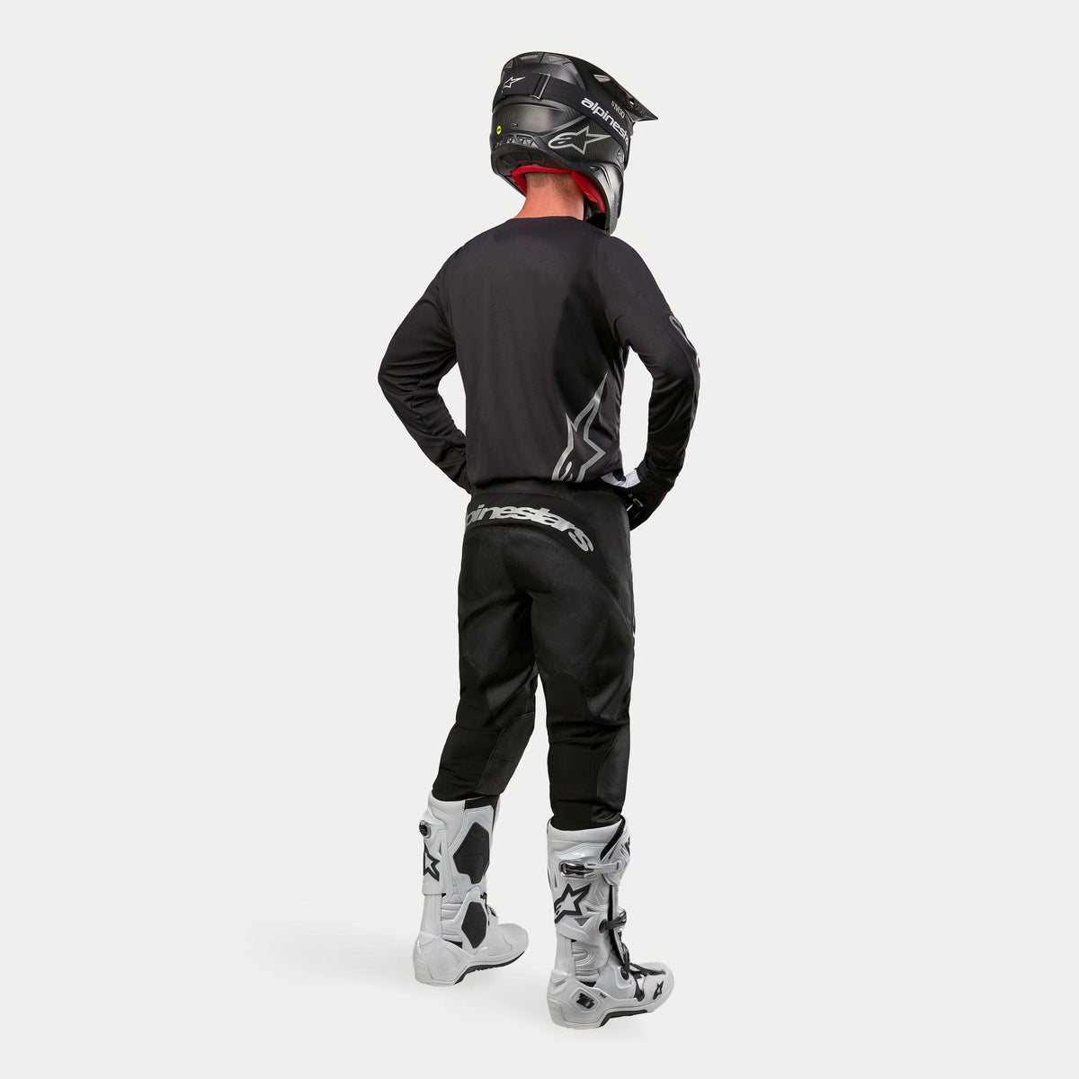 Alpinestars 2024 Fluid Graphite Hose, Motocross-Hose, Schwarz und Silber, Rückansicht eines Fahrers mit schwarzem Jersey, schwarzem Helm und weiß-schwarzen Stiefeln, silbernes Branding am unteren Rücken, strapazierfähige Poly-Gewebe-Konstruktion für Offroad-Rennsport