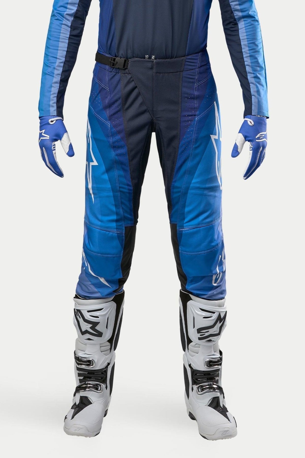 Alpinestars Techstar Pneuma Pants 2024, pantalon de motocross, bleu marine et bleu clair, porté avec un maillot bleu assorti et des bottes blanches, avec logo Alpinestars blanc et boucle de fermeture magnétique, conçu pour la performance tout-terrain professionnelle