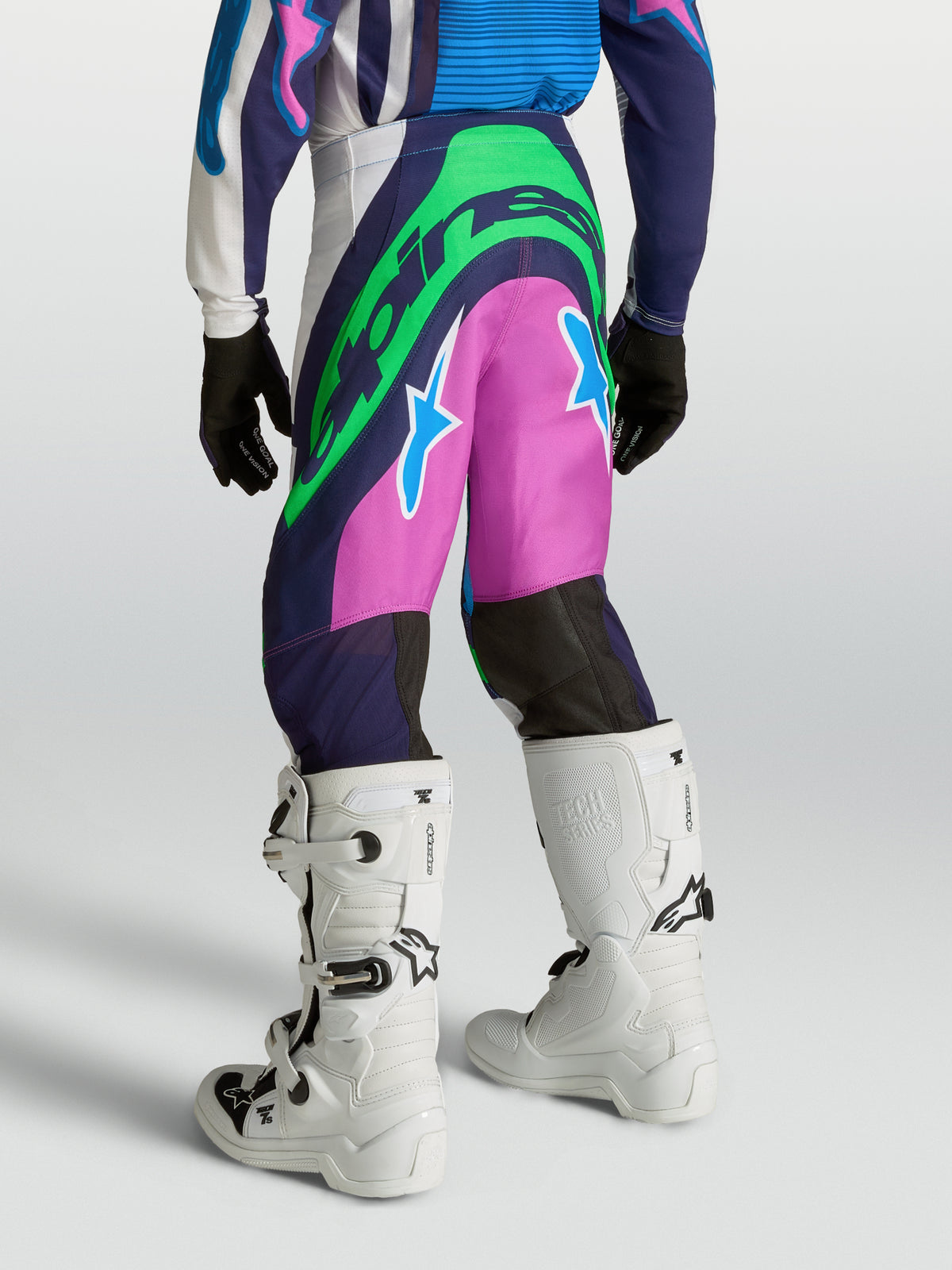 Alpinestars Jeugd Supertech Maven broek, blauw-roze motorcrossbroek met neongroene logo's, atletische racepasvorm op model.