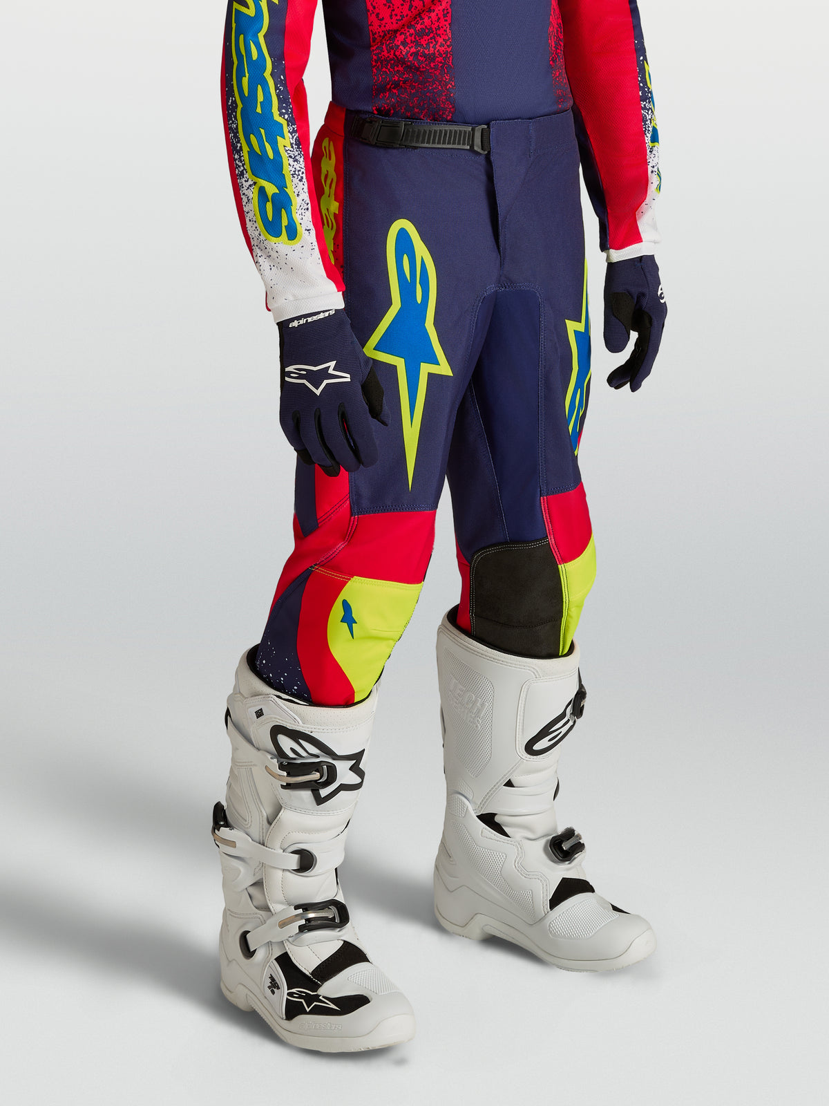 Alpinestars pantalon Fluid Drag Junior 2027, pantalon de motocross bleu marine et rouge avec accents néon et bottes blanches.