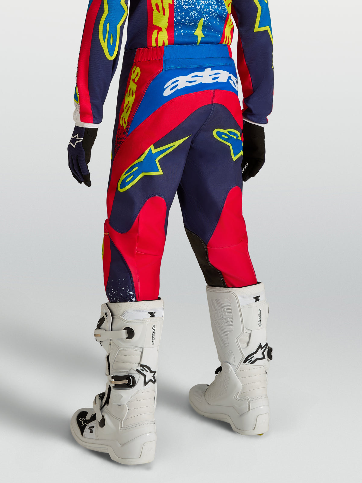 Alpinestars Pantalon Fluid Drag Junior, pantalon de motocross pour enfant, bleu marine et rouge feu, vue de dos avec des bottes blanches, conçu pour la performance en tout-terrain.