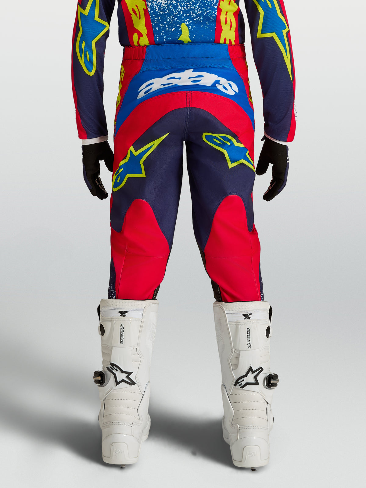 Alpinestars Fluid Drag Junior, pantalon de motocross pour enfant, bleu marine et rouge, en textile 600D avec coupe ergonomique arrière, vue de dos montrant l'ajustement performance et les détails graphiques.