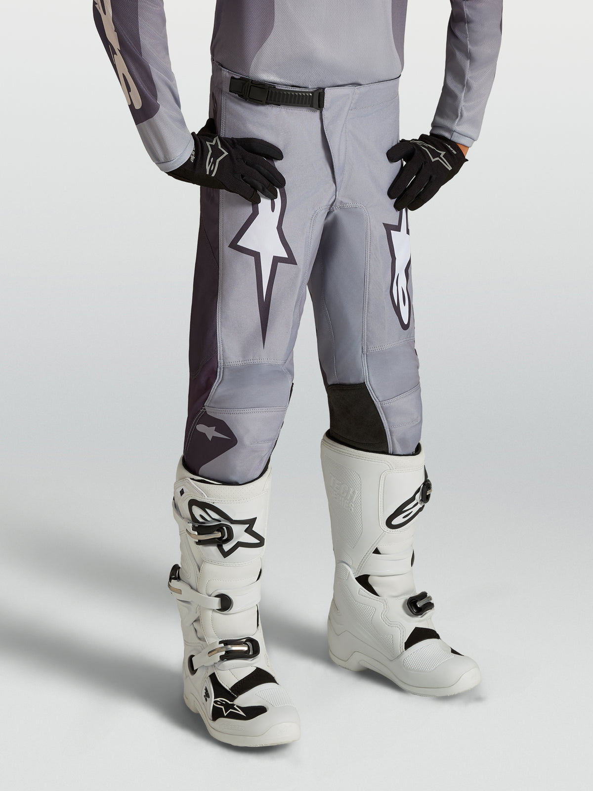 Pantalon Alpinestars Fluid Amber Junior, pantalon de motocross pour junior, gris sable et blanc, avec graphismes d'étoiles et panneaux renforcés, porté par un mannequin.