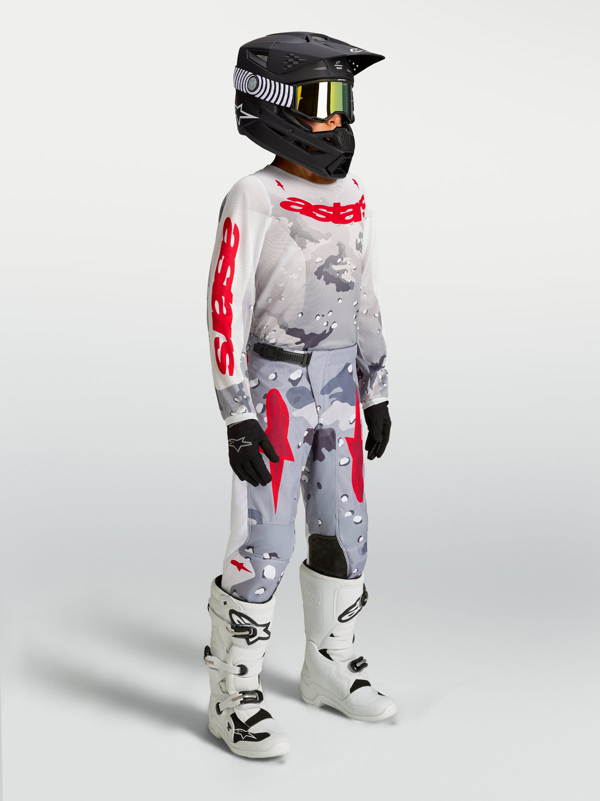 Alpinestars pantalon Fluid Lone Junior, pantalon de motocross junior, camouflage gris et rouge feu, textile 600D à coupe ergonomique, porté par un jeune pilote.