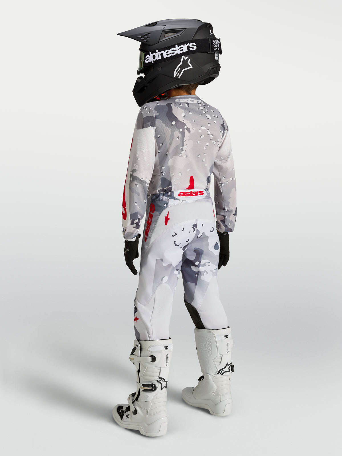 Alpinestars Fluid Lone Junior, pantalon de motocross gris camouflage et blanc avec rouge, vue de dos sur jeune pilote.