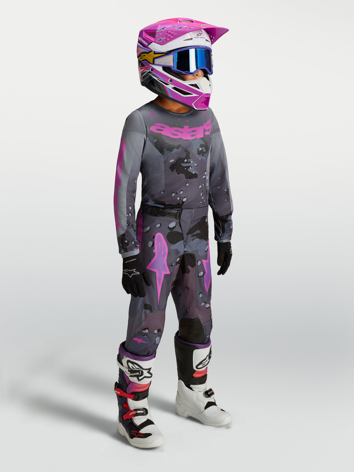 Alpinestars Jeune Fluid Lone Gear Set, tenue de motocross junior grise et rose, comprenant un maillot et un pantalon ergonomiques portés par un pilote pour le tout-terrain.