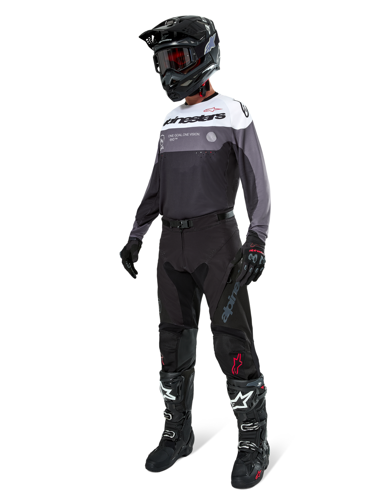 Maillot Alpinestars Pro-Dura en Black Magnet White, porté par un pilote de motocross en tenue complète avec un pantalon noir, un casque noir avec lunettes et des bottes noires et blanches. Le maillot présente un design technique color-block avec des panneaux blancs, gris et noirs, conçu pour la performance en enduro et en tout-terrain.