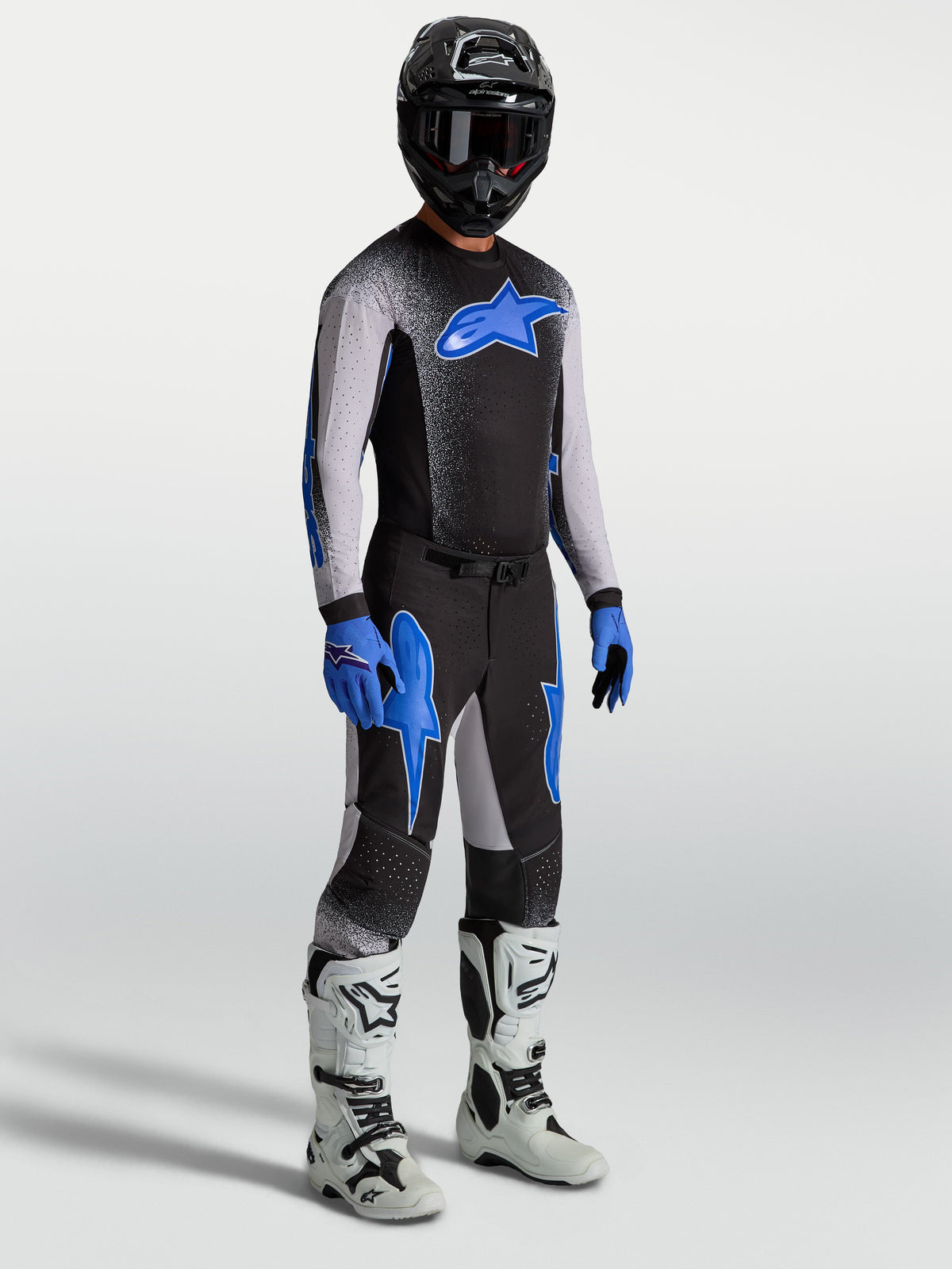 Alpinestars Supertech Hiten AFD Jersey en Supertech Hiten AFD Gear Set, zwart en blauwe motocrossuitrusting met witte motorlaarzen en zwarte helm.