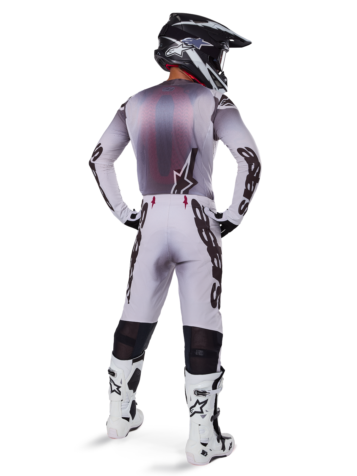 Motorcrossrijder van achteren gezien in de 2025 Supertech Maker Gear Set in het wit, voorzien van een grijs en witte jersey met zwarte Alpinestars-branding, bijpassende motorcrossbroek, wit-zwarte laarzen en een zwarte helm, gecoördineerde off-road race-uitrusting