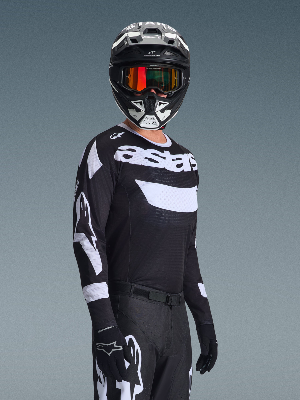 Pilote de motocross portant le maillot Racer Air Riway 2026, maillot noir et blanc avec le logo 'astars', casque assorti noir et blanc avec lunettes miroir orange, pantalon et gants de motocross noirs, tenue coordonnée pour la course tout-terrain