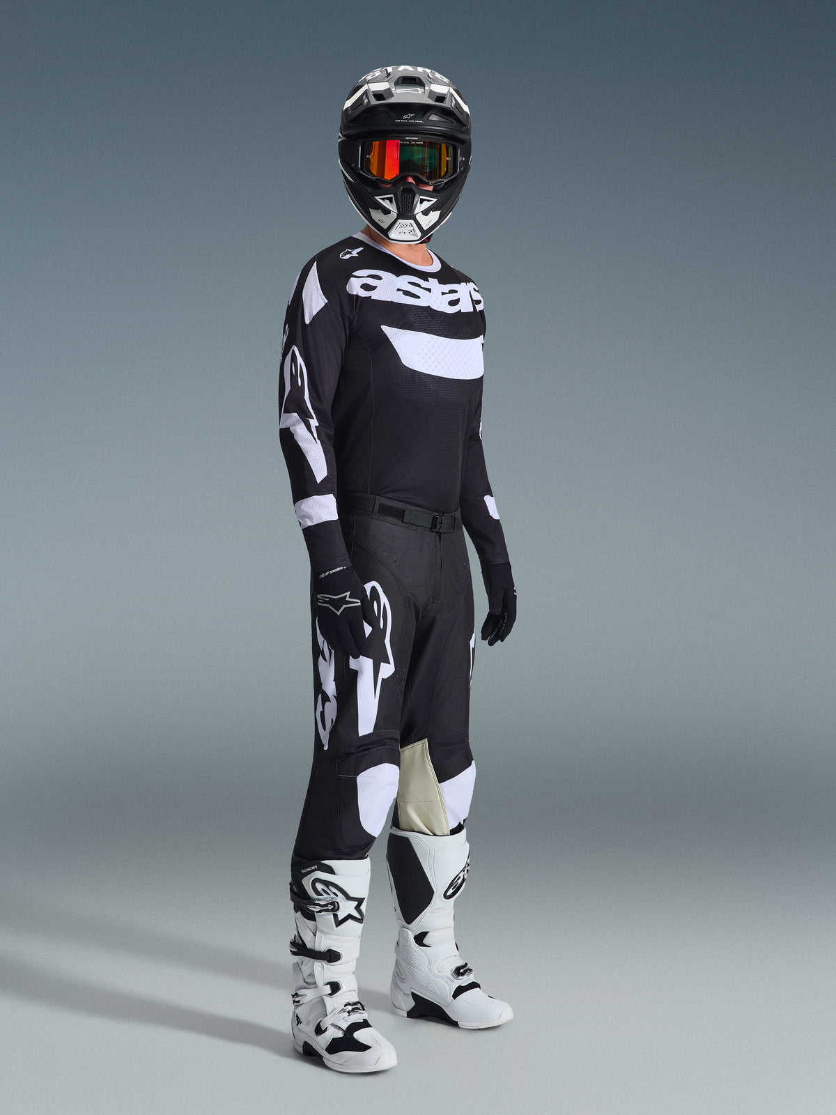 Alpinestars 2026 Racer Air Riway Bekleidungsset, Motocross-Fahrer in kompletter Rennausrüstung, schwarzes Jersey mit weißem 'Astars'-Branding und Mesh-Einsätzen, schwarze Hose mit großen weißen Logos und Knie-Einsätzen, schwarzer Helm mit roter Brille, weiß-schwarze Stiefel, professionelles Offroad-Rennoutfit.