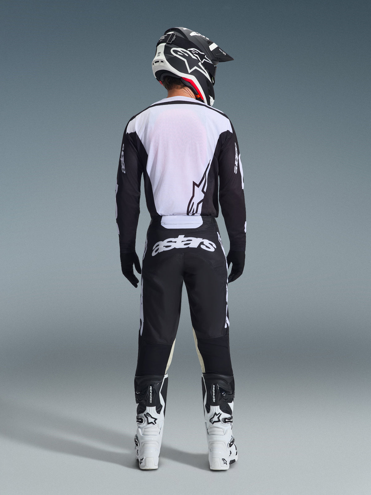Alpinestars 2026 Racer Air Riway Gear Set, Motocross-Ausrüstung, Schwarz und Weiß, Rückansicht eines Fahrers in belüftetem Jersey mit weißen Mesh-Paneelen, passende Hose mit markantem Astars-Branding am Gesäß, kombiniert mit weiß-schwarzen Motocross-Stiefeln und Helm