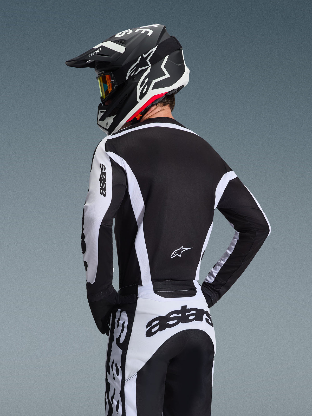 Motocross rider from behind wearing the Alpinestars 2026 Racer Riway Jersey in White and Black, featuring 'astars' branding on the sleeves and lower back, paired with matching motocross pants and a black helmet with goggles, coordinated gear for off-road racing.