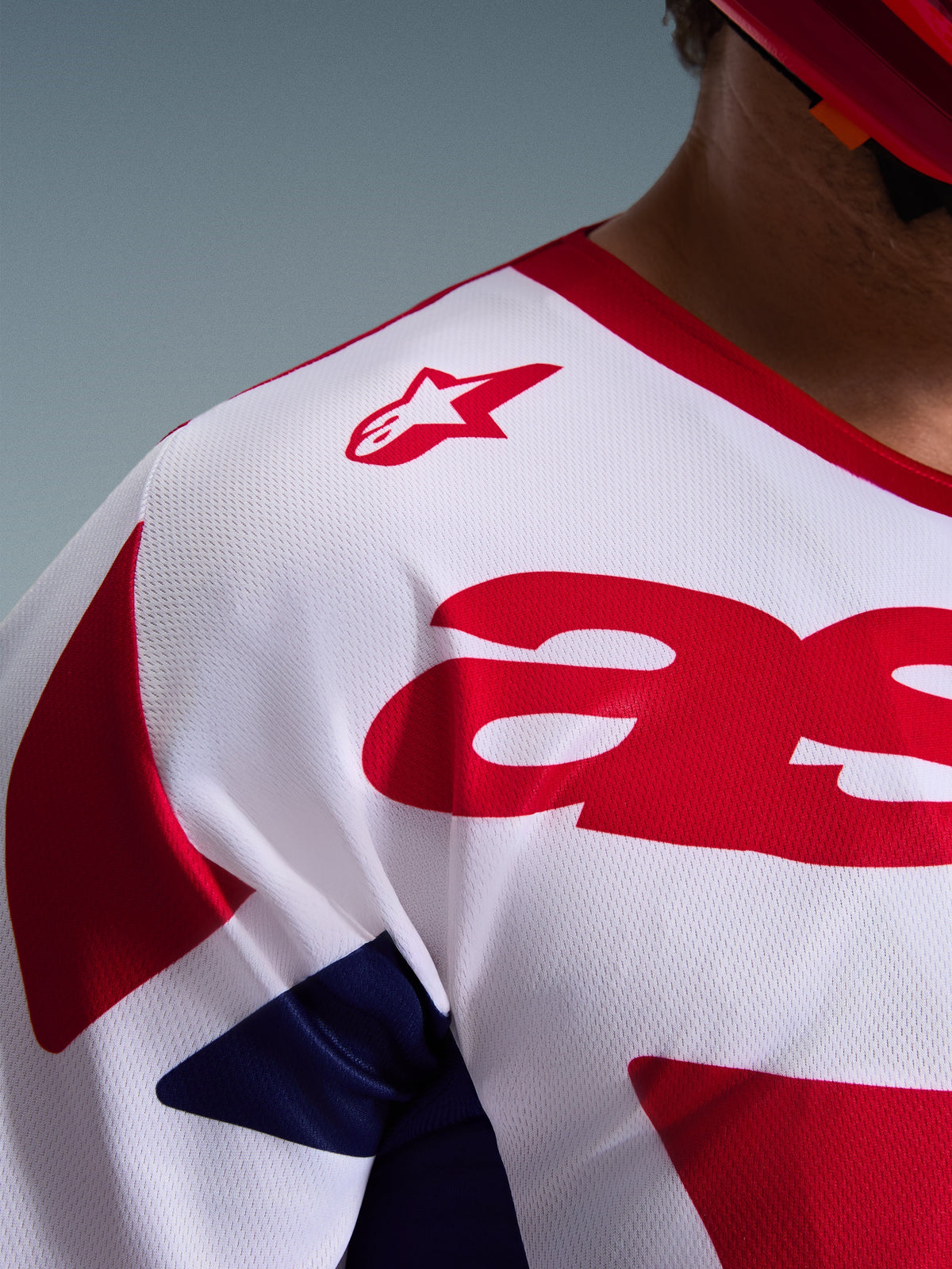 Détail rapproché du maillot Alpinestars Racer Riway 2026 en blanc, bleu et rouge, mettant en avant la construction en poly-tissu maillé respirant, le logo Alpinestars rouge sur l'épaule et le matériau évacuant l'humidité pour le tout-terrain.