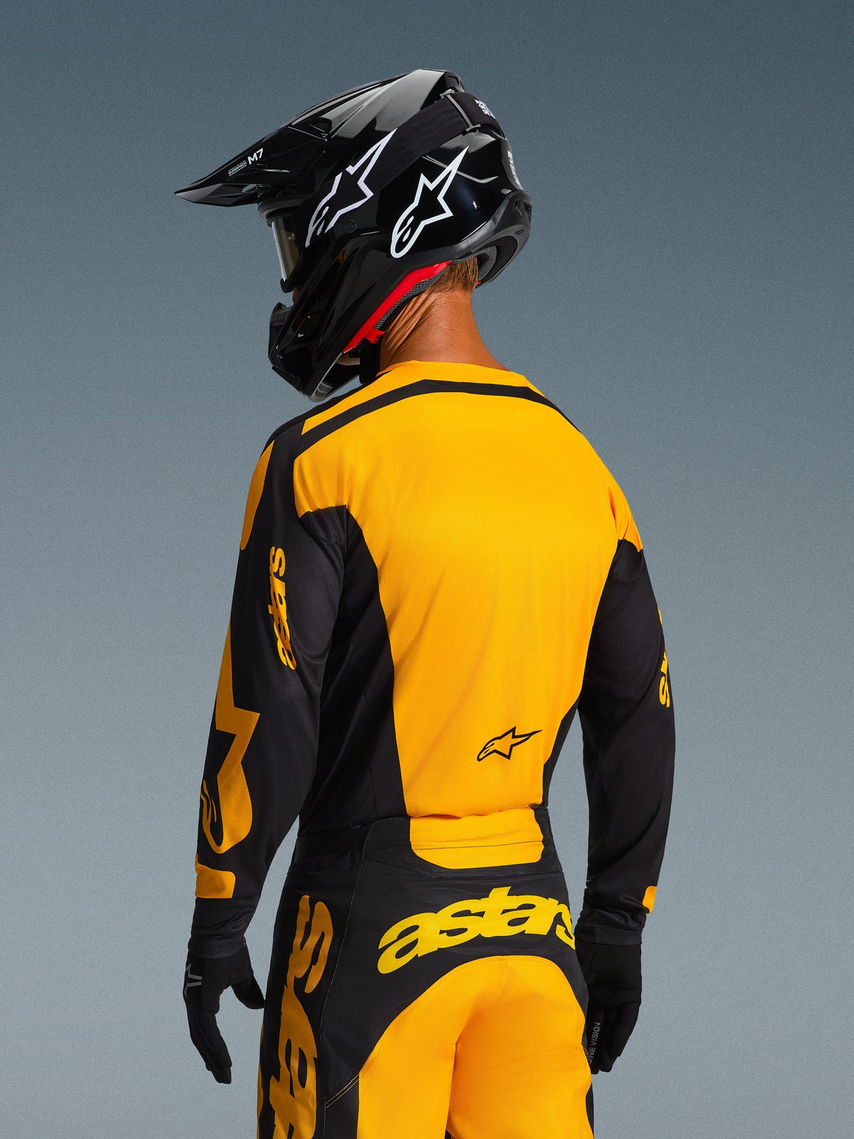 Alpinestars 2026 Racer Riway Jersey in geel en zwart, achteraanzicht van een motorcrosser, opvallend geel rugpaneel en zwarte mouwen met gele logo's, gecombineerd met bijpassende motorcrossbroek en zwarte helm, complete off-road race-uitrusting