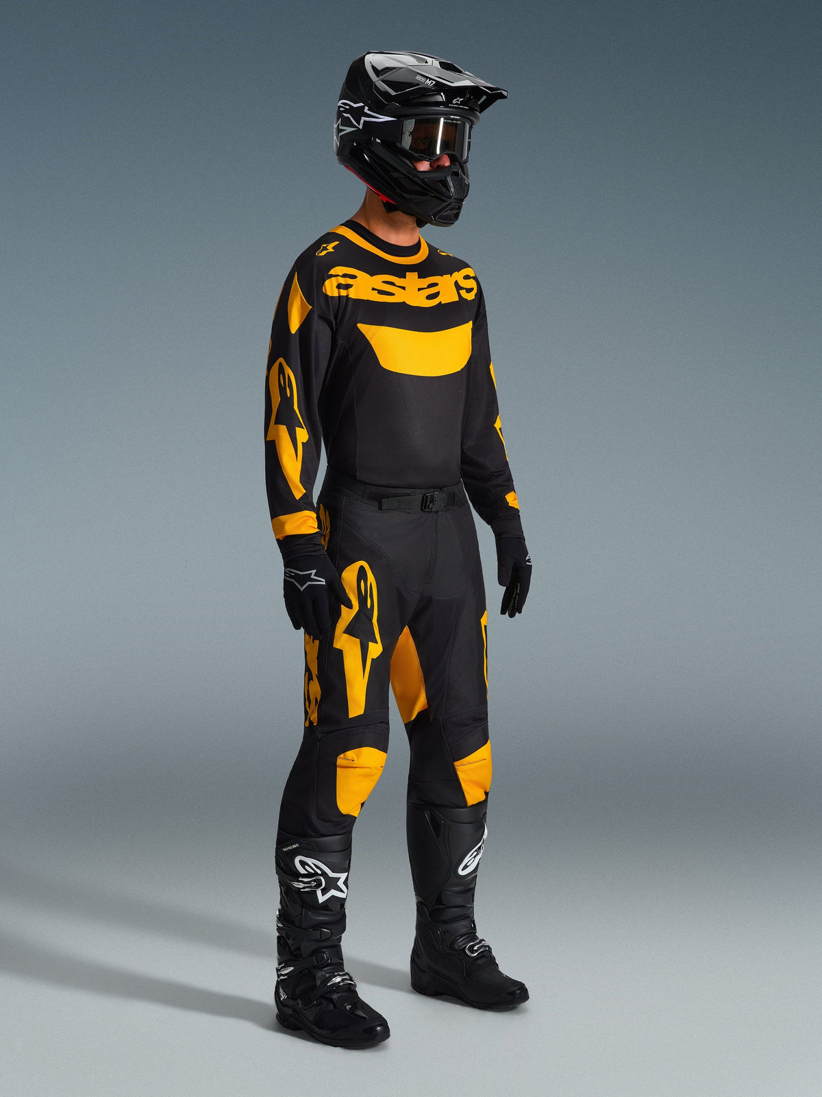 Alpinestars 2026 Racer Riway Jersey in geel en zwart, motorcrossrijder in een complete race-uitrusting met bijpassende broek, zwarte helm, handschoenen en laarzen, ontworpen voor off-road prestaties met opvallende Alpinestars graphics.