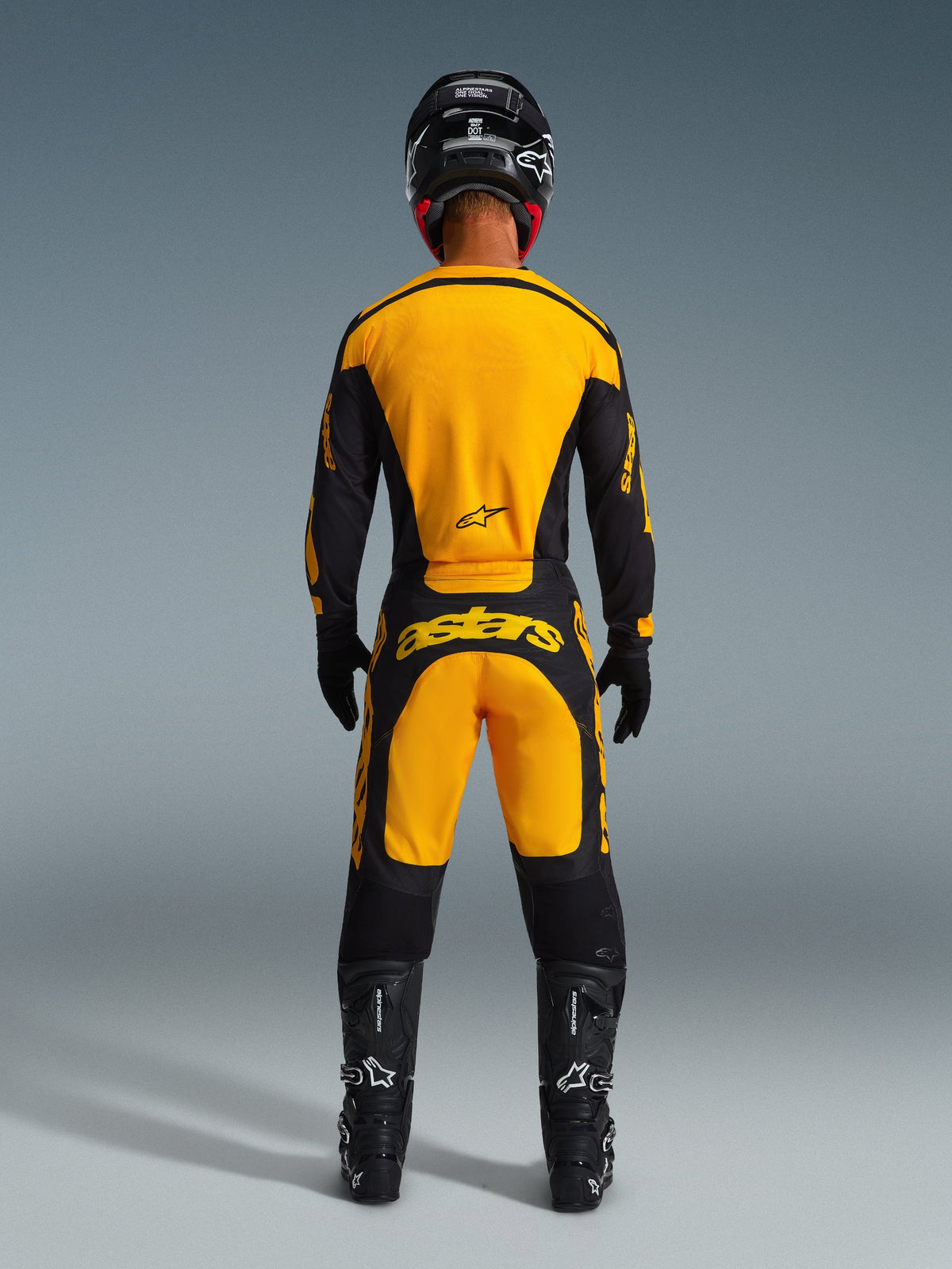 Alpinestars motorcrosser van achteren gezien in de 2026 Racer Riway Jersey en bijpassende broek, geel en zwart, zwarte helm, laarzen en handschoenen, volledige off-road race-uitrusting met opvallende branding.