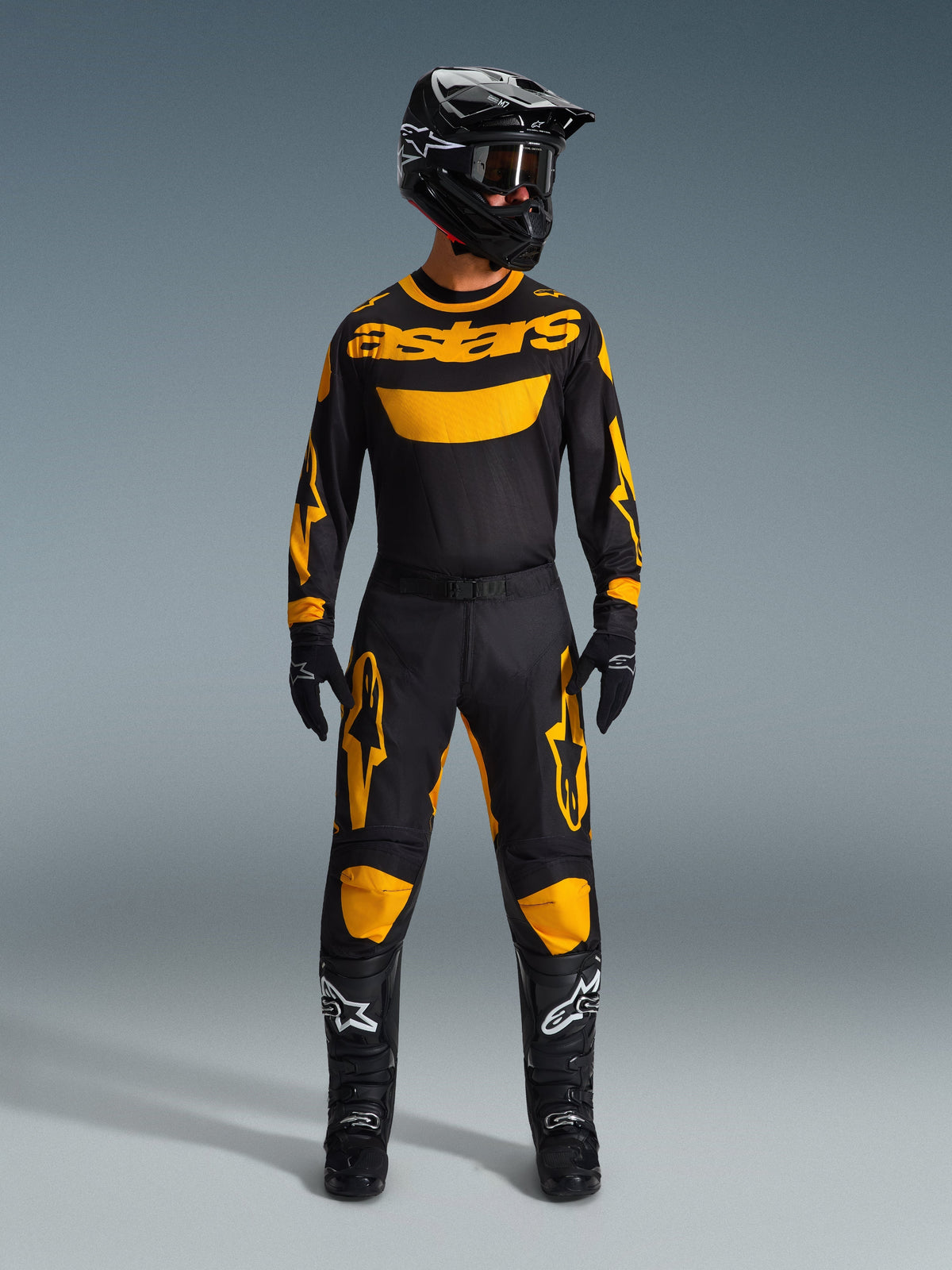 Motorcrosser draagt de 2026 Racer Riway Jersey in geel en zwart, gecombineerd met bijpassende broek, zwarte helm en zwarte laarzen met witte Alpinestars-logo's, volledige uitrusting voor off-road racing.