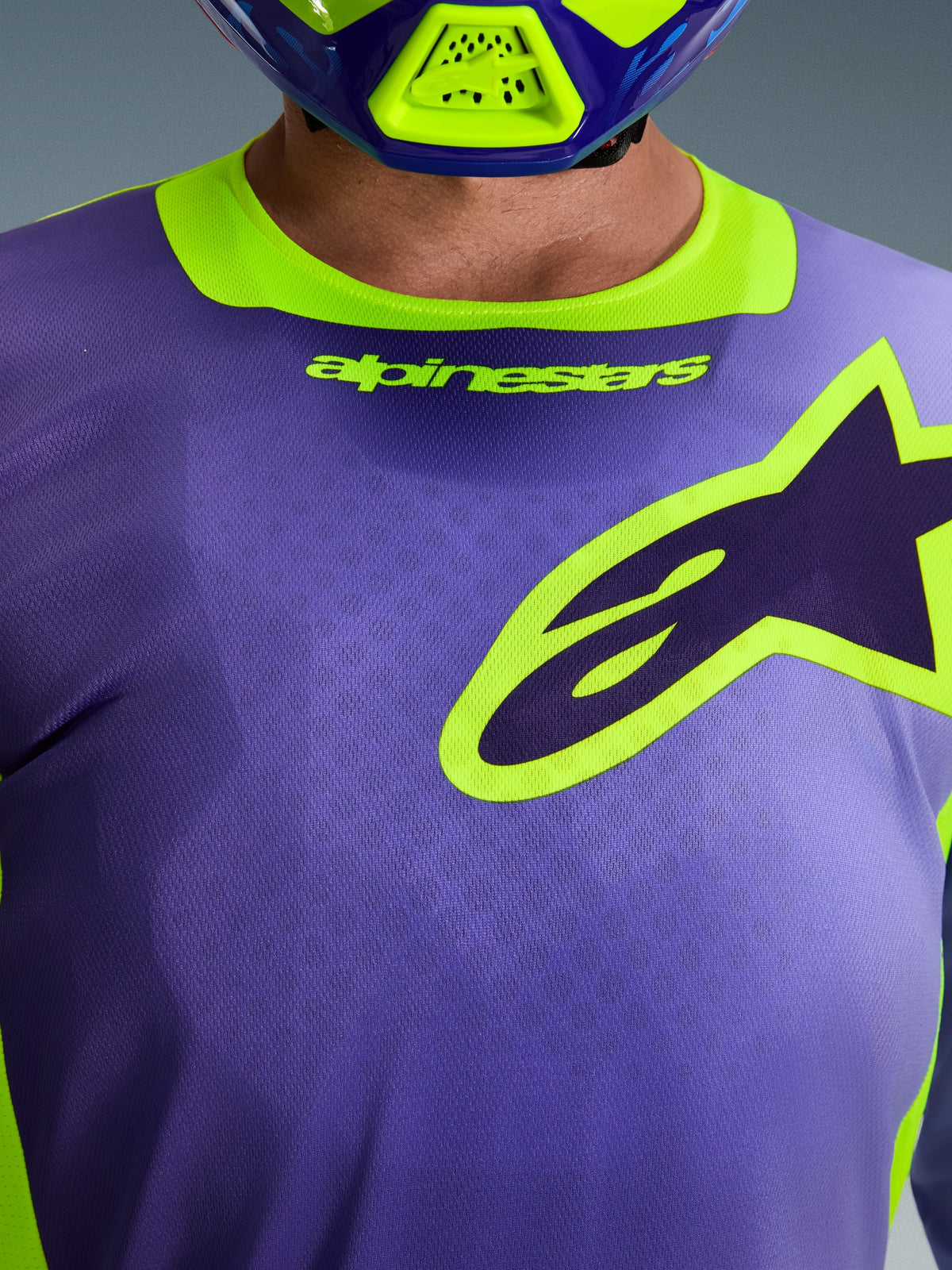 Maillot Alpinestars Racer Portl 2026, violet et jaune fluo, gros plan sur la poitrine et le col présentant le lettrage Alpinestars et le logo de l'étoile, porté avec un casque de motocross assorti, vêtement technique de course tout-terrain.